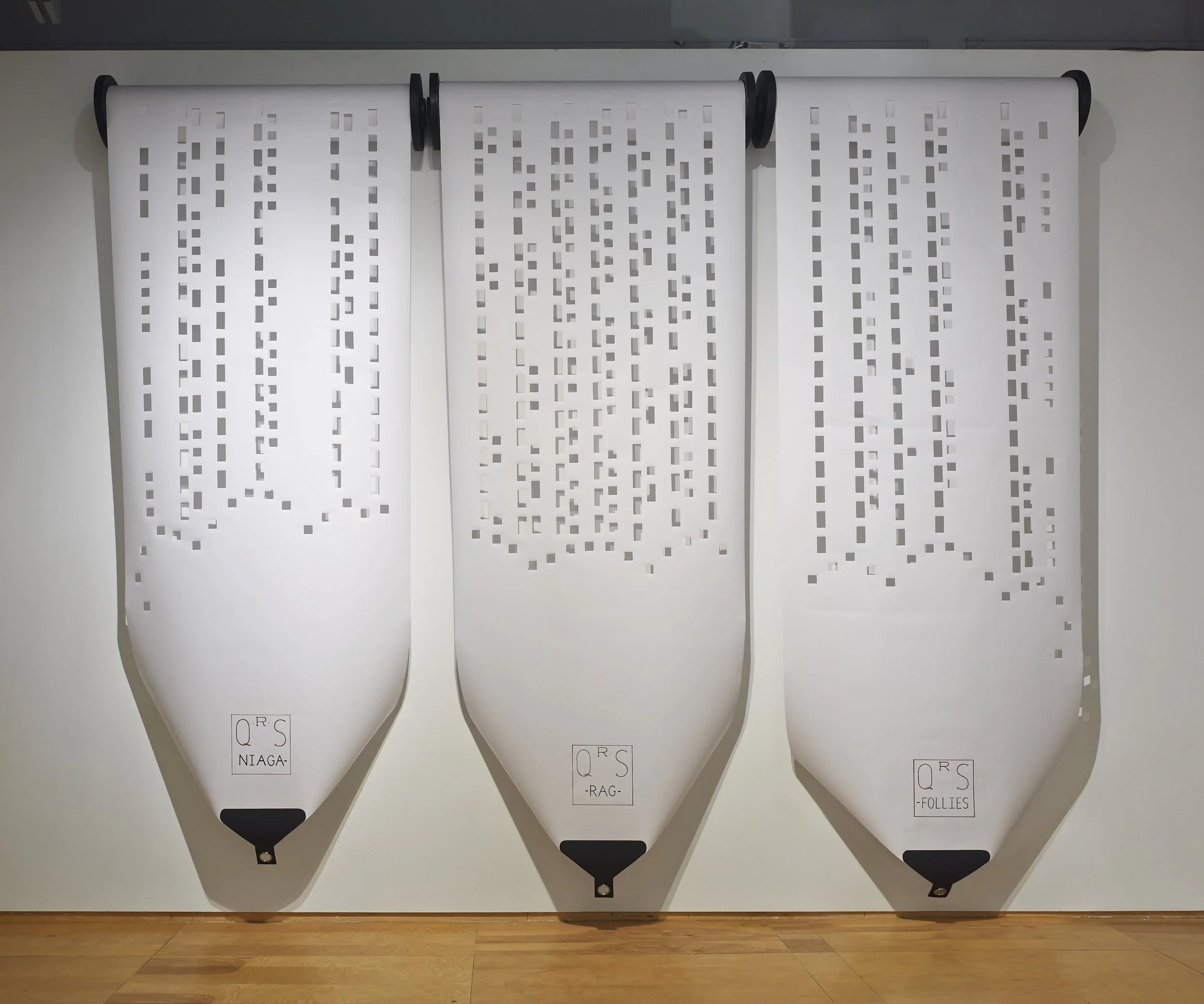 Three white banners with perforated geometric patterns hanging on a wall, labeled 'NIAGA', 'RAG', and 'FOUILLES' at the bottom.