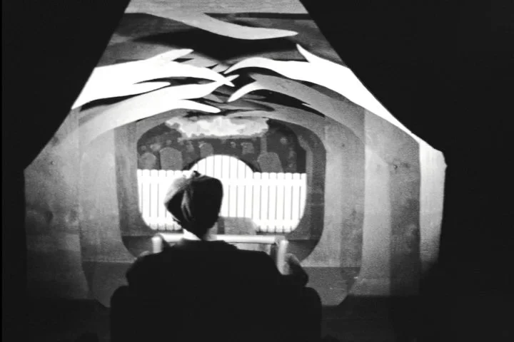 A person sitting in front of a circular window with fish sculptures hanging from the ceiling.