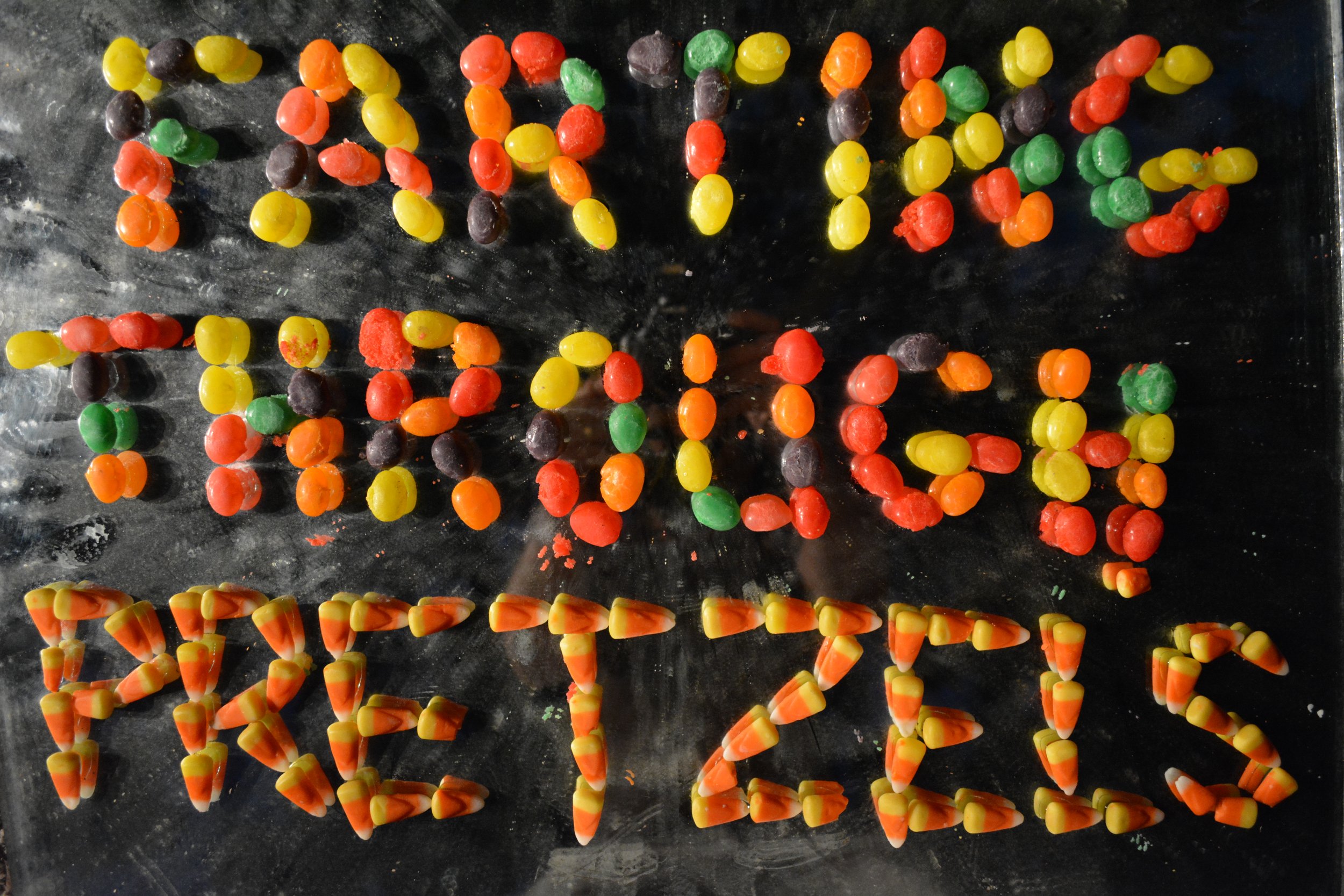 Colorful jelly beans arranged on a black surface to spell out "HAPPY HALLOWEEN" and "RULES".