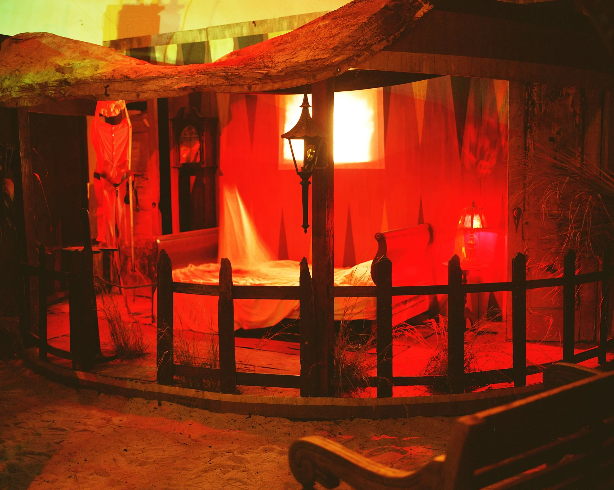 A spooky room decorated as a haunted house scene with a bed, dim lighting, a black fence, and red lighting, creating a sinister atmosphere.