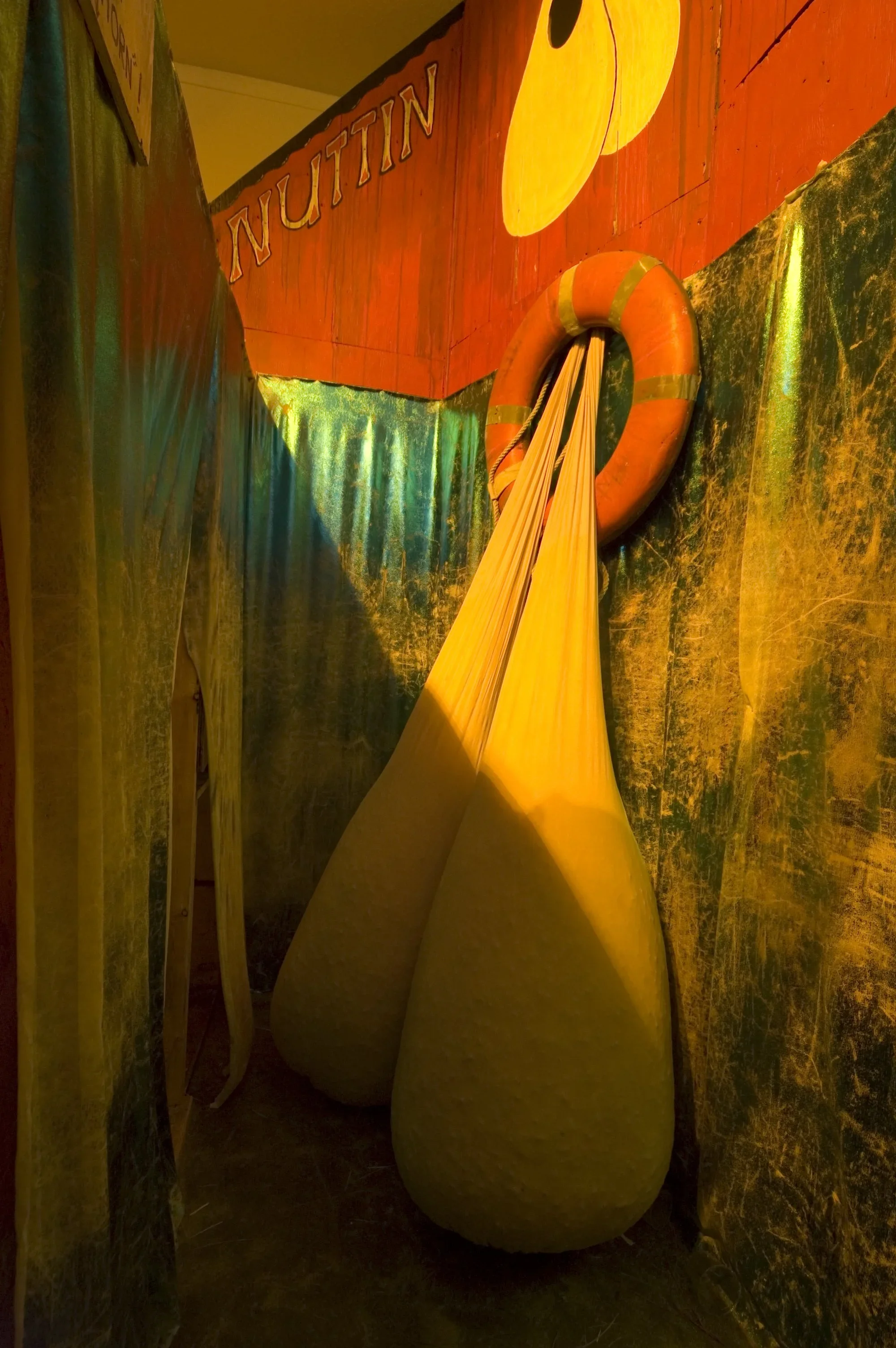 Indoor exhibit with two large yellow flotation devices resembling the shape of pears, hanging from a life preserver mounted on a colorful, textured wall with the word 'NUTRITION' painted on it.