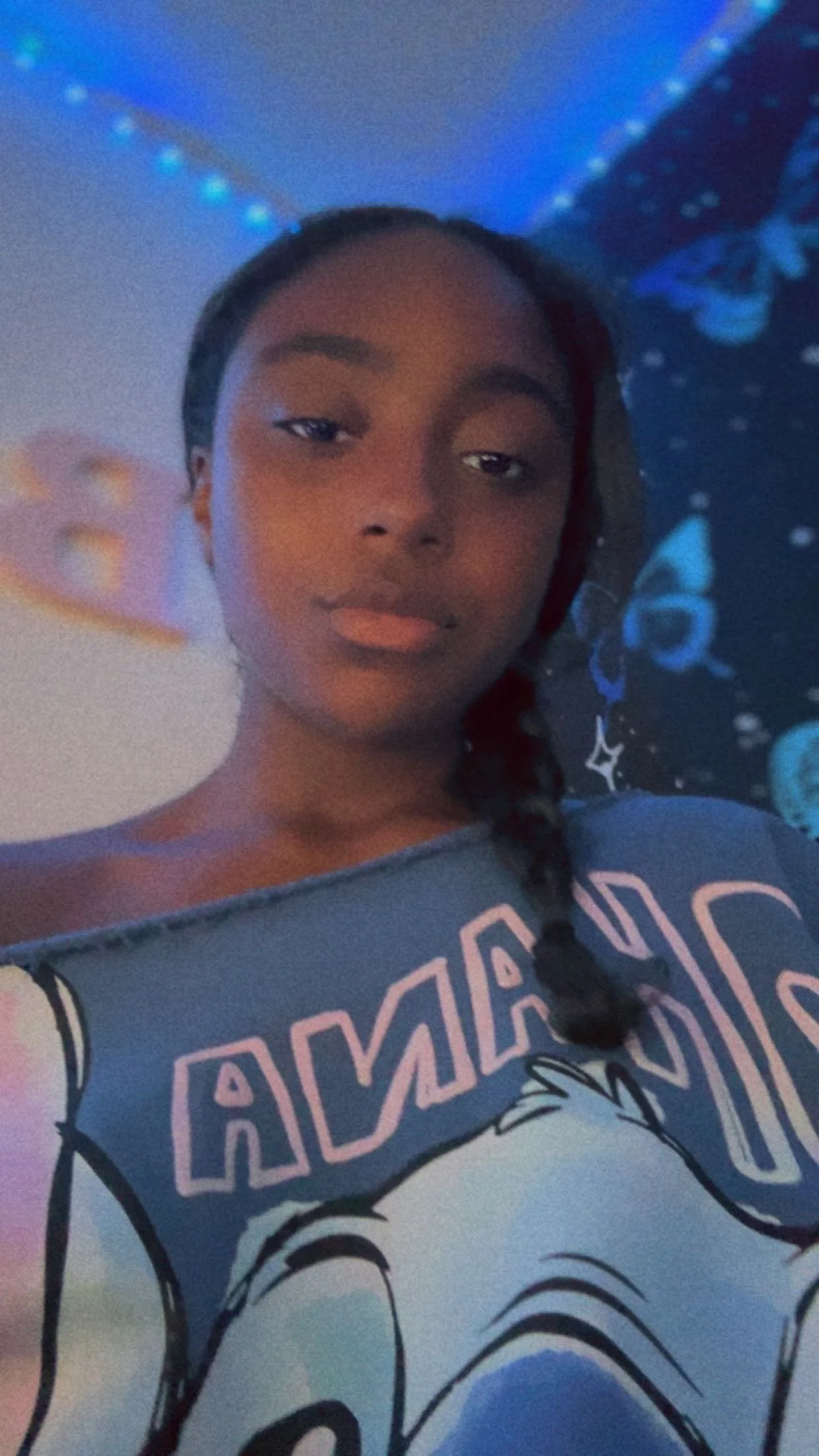 A young woman taking a selfie in a room with galaxy-themed decorations on the wall and a ceiling light strip.