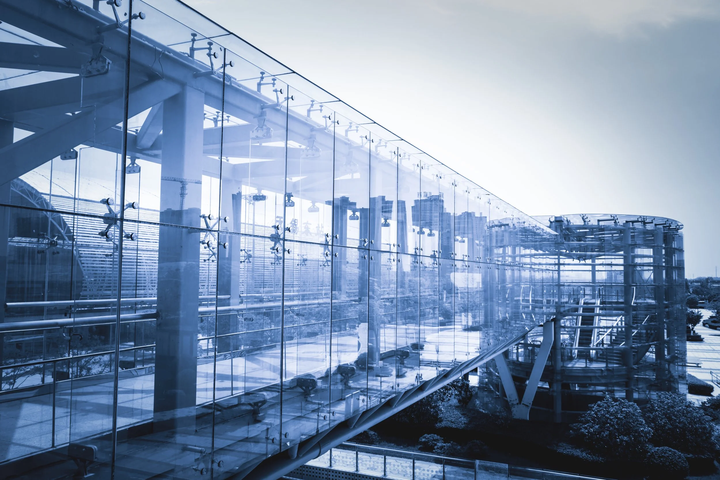 Modern glass building with visible steel beams and a crane in the city background.