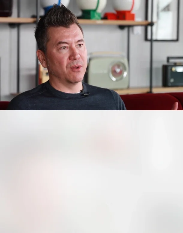 A man sat in a couch with office background speaking to the camera