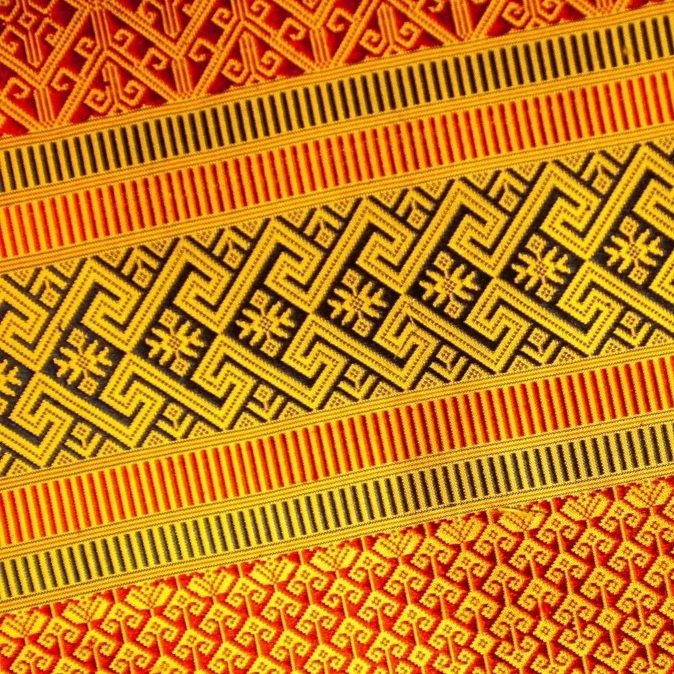 Close-up of woven fabric with geometric and floral patterns in red, yellow, and black colors.