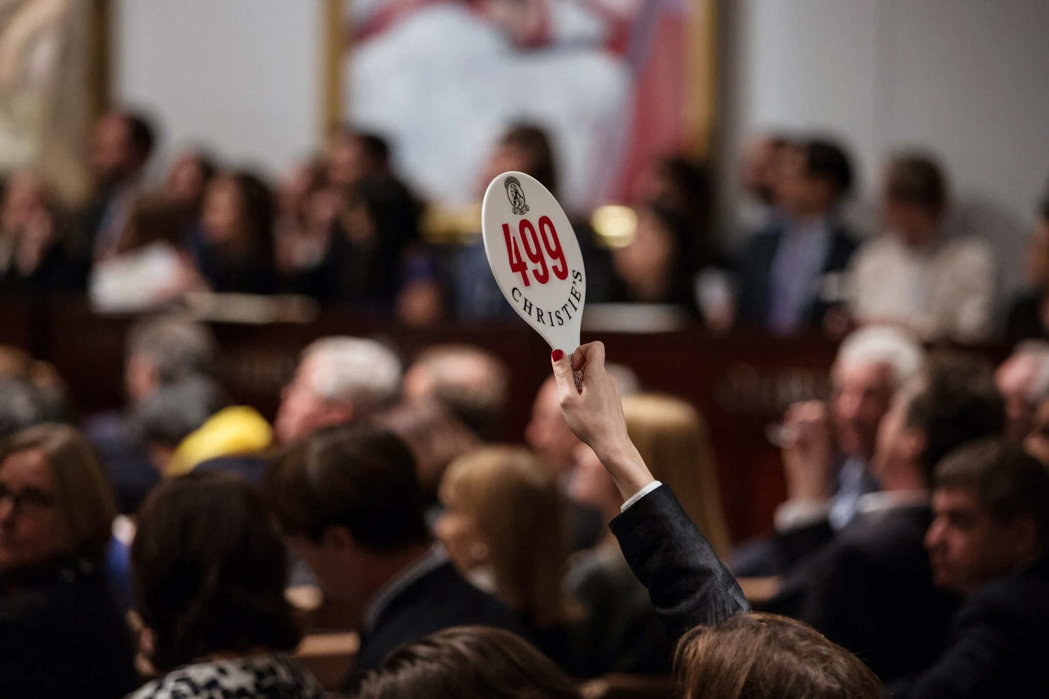 Person raising a paddle with the number 217 during an auction, surrounded by seated audience members.