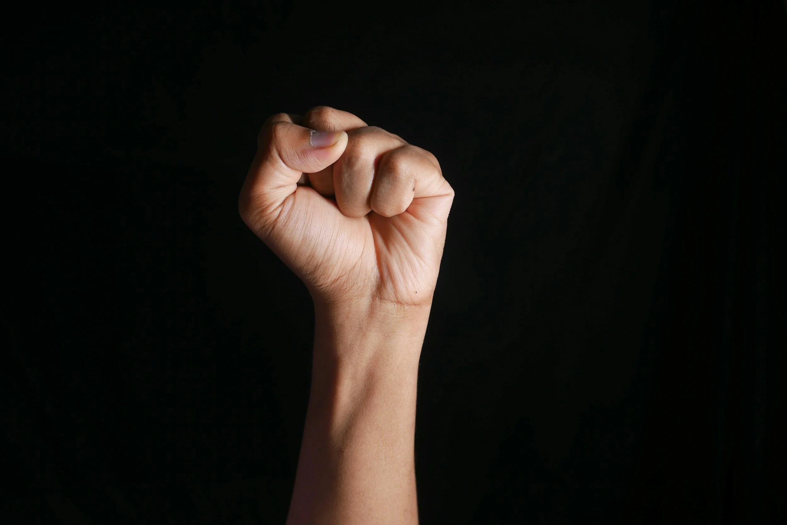 A clenched fist raised against a dark background.