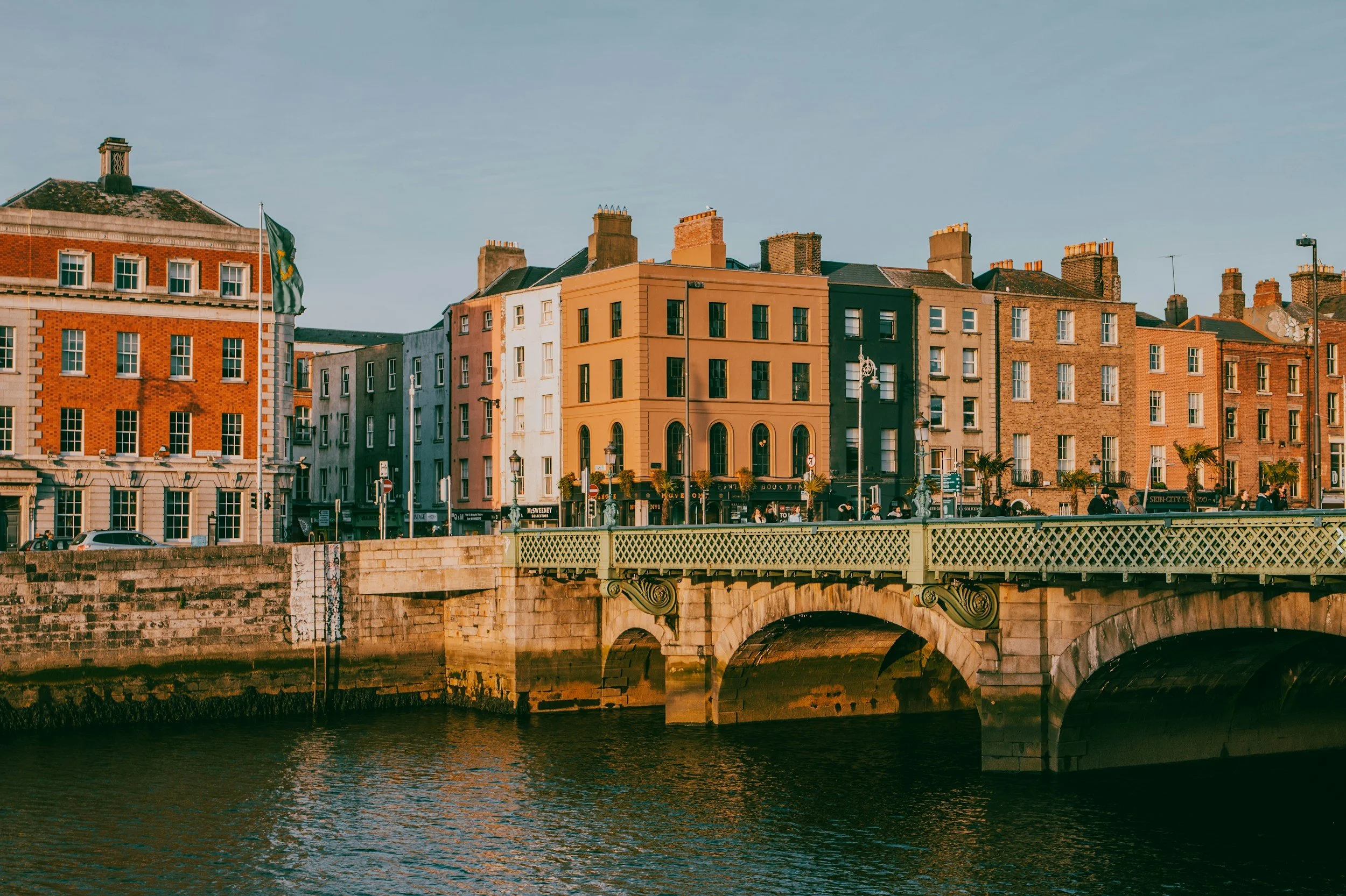 Colorful buildings along the rive Liffey in Dublin  with a stone bridge in the foreground, under a clear sky.