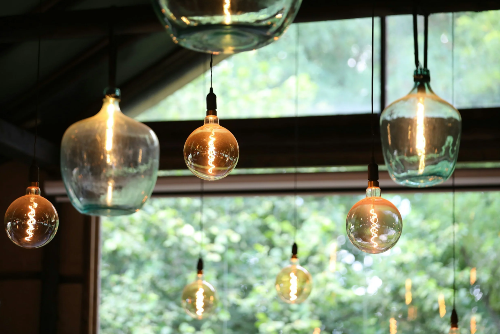 Pendant lights with Edison bulbs hanging indoors near a window with trees outside.