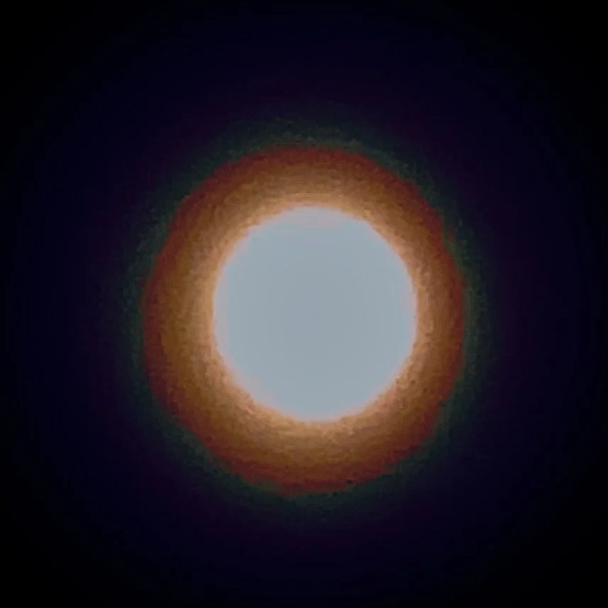 Bright white circular light with a reddish-orange halo surrounding it, set against a dark background.