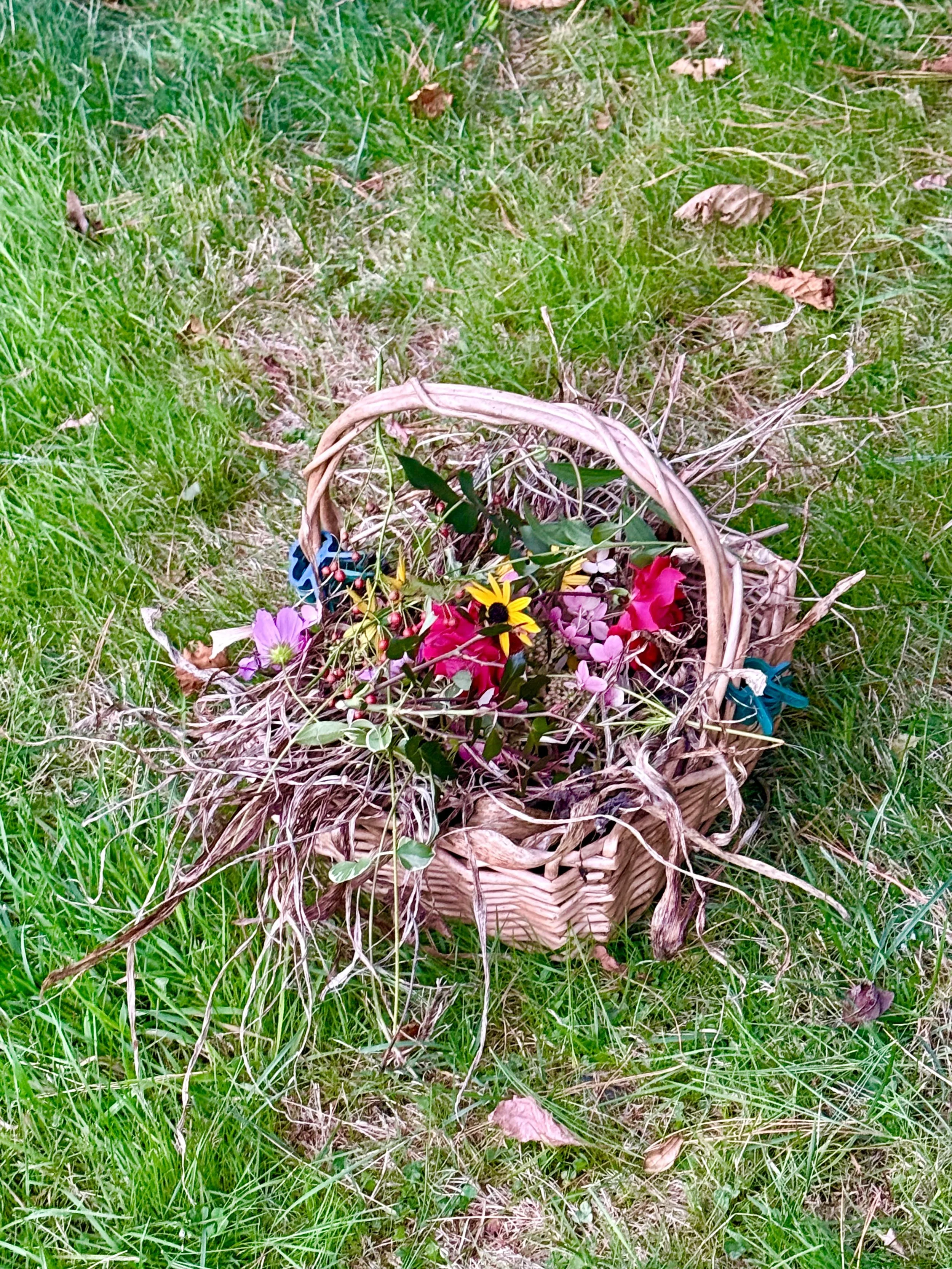 A basket filled with colorful flowers on a grassy area outdoors.