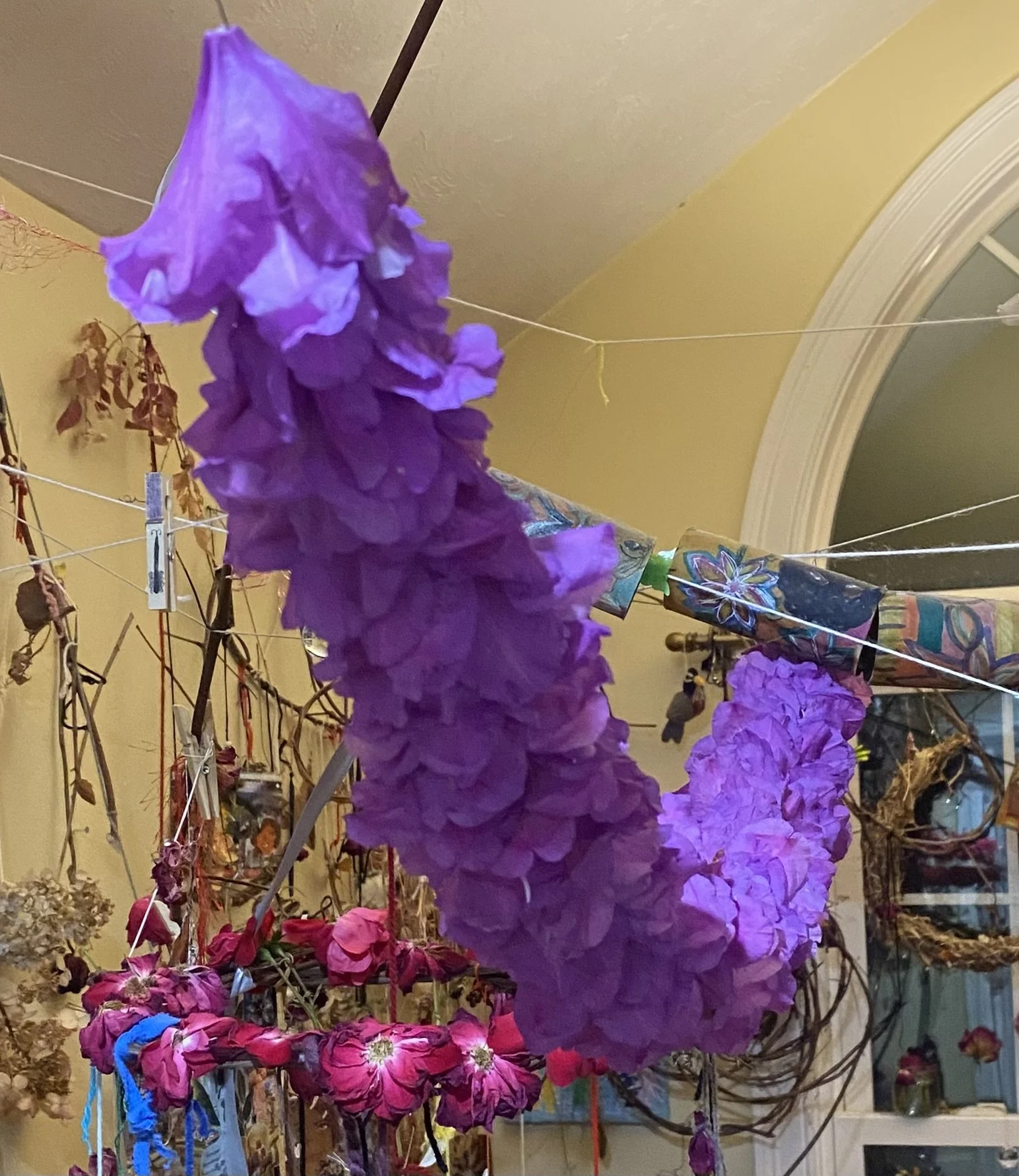 Hanging purple and pink dried flowers and artwork in a room with yellow walls.
