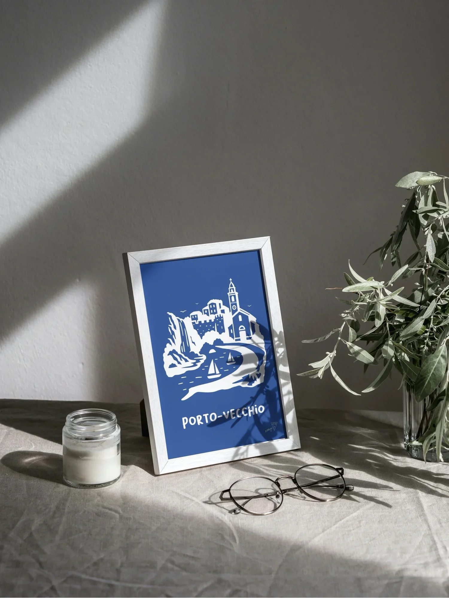 Affiche Porto-Vecchio encadrée dans un intérieur lumineux, illustration bleu et blanche de la ville Corse