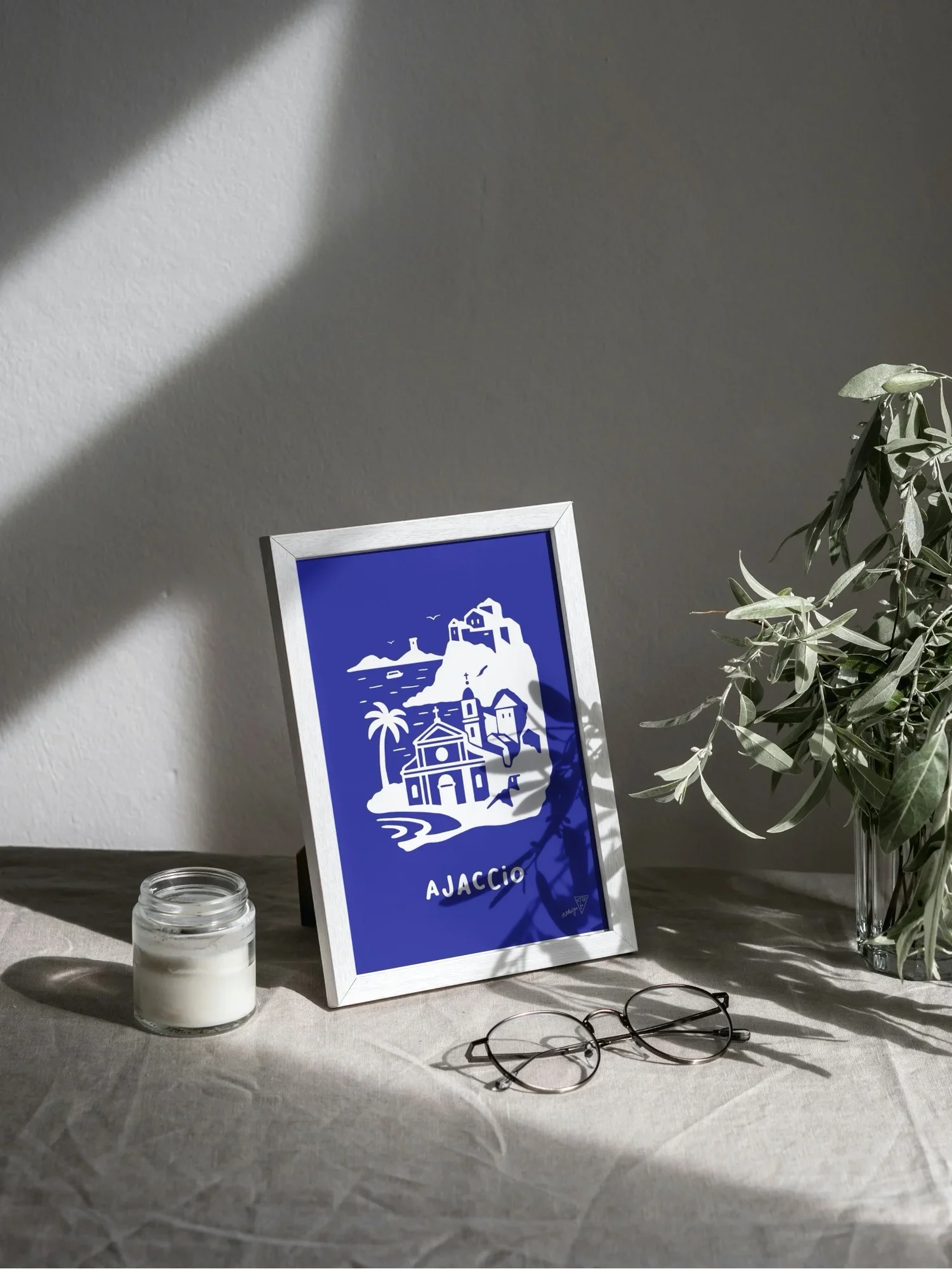 Affiche Ajaccio encadrée dans un intérieur lumineux, illustration bleu et blanche de la ville Corse