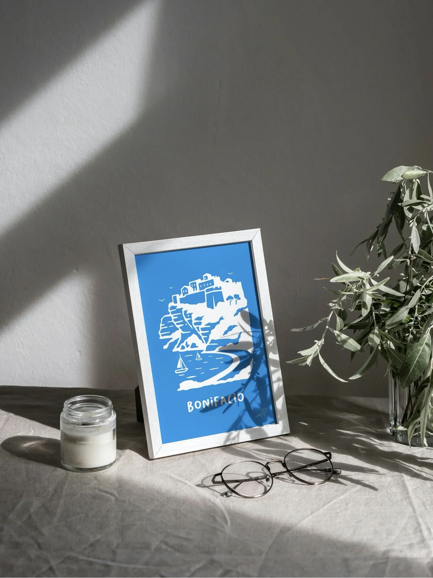 Affiche Bonifacio encadrée dans un intérieur lumineux, illustration bleu et blanche de la ville Corse