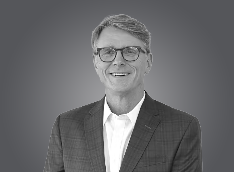 A smiling middle-aged man with glasses, wearing a checkered blazer and a white shirt, against a neutral background.