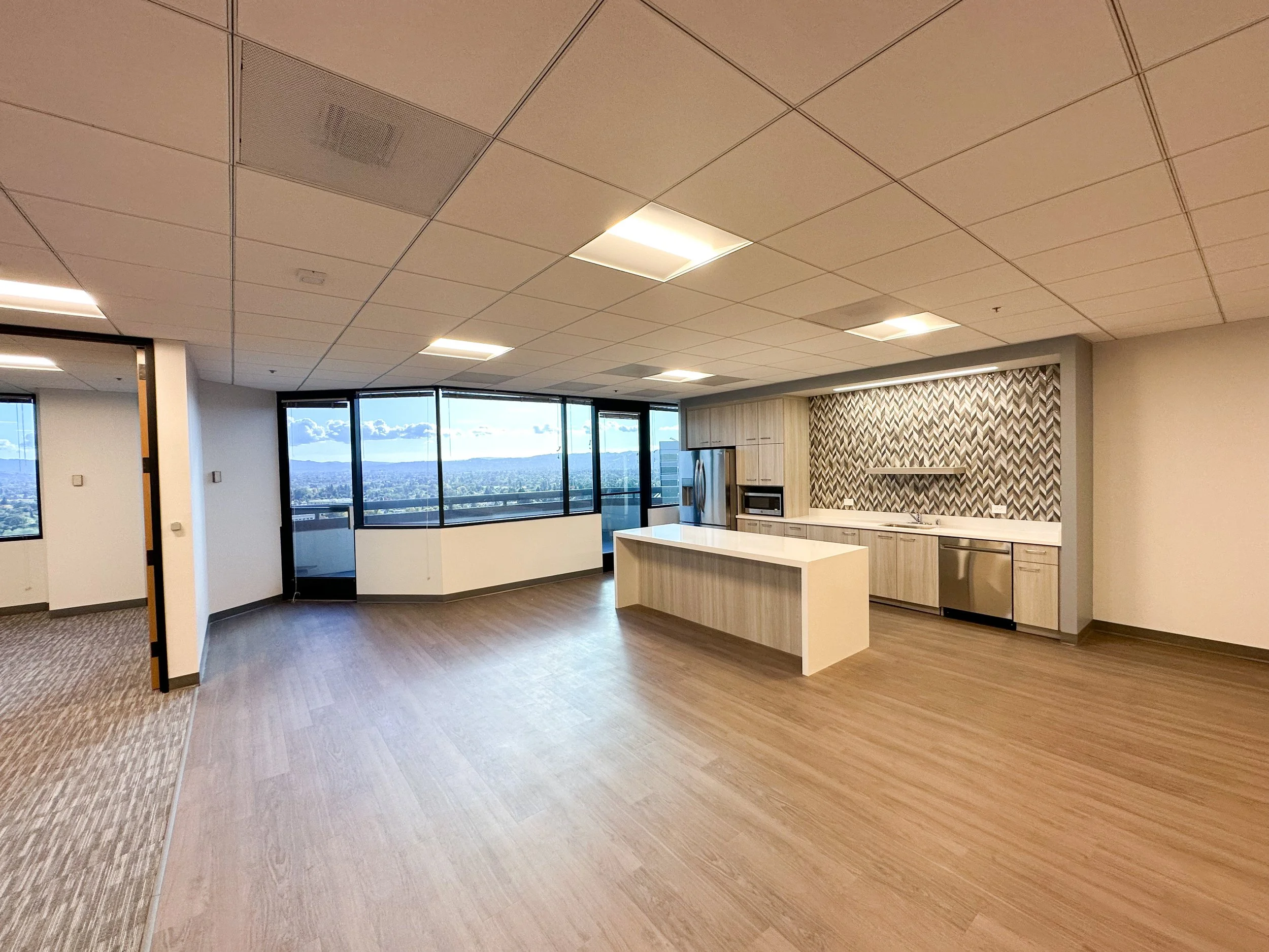 Spacious modern apartment kitchen with large windows, wooden flooring, and a patterned backsplash.