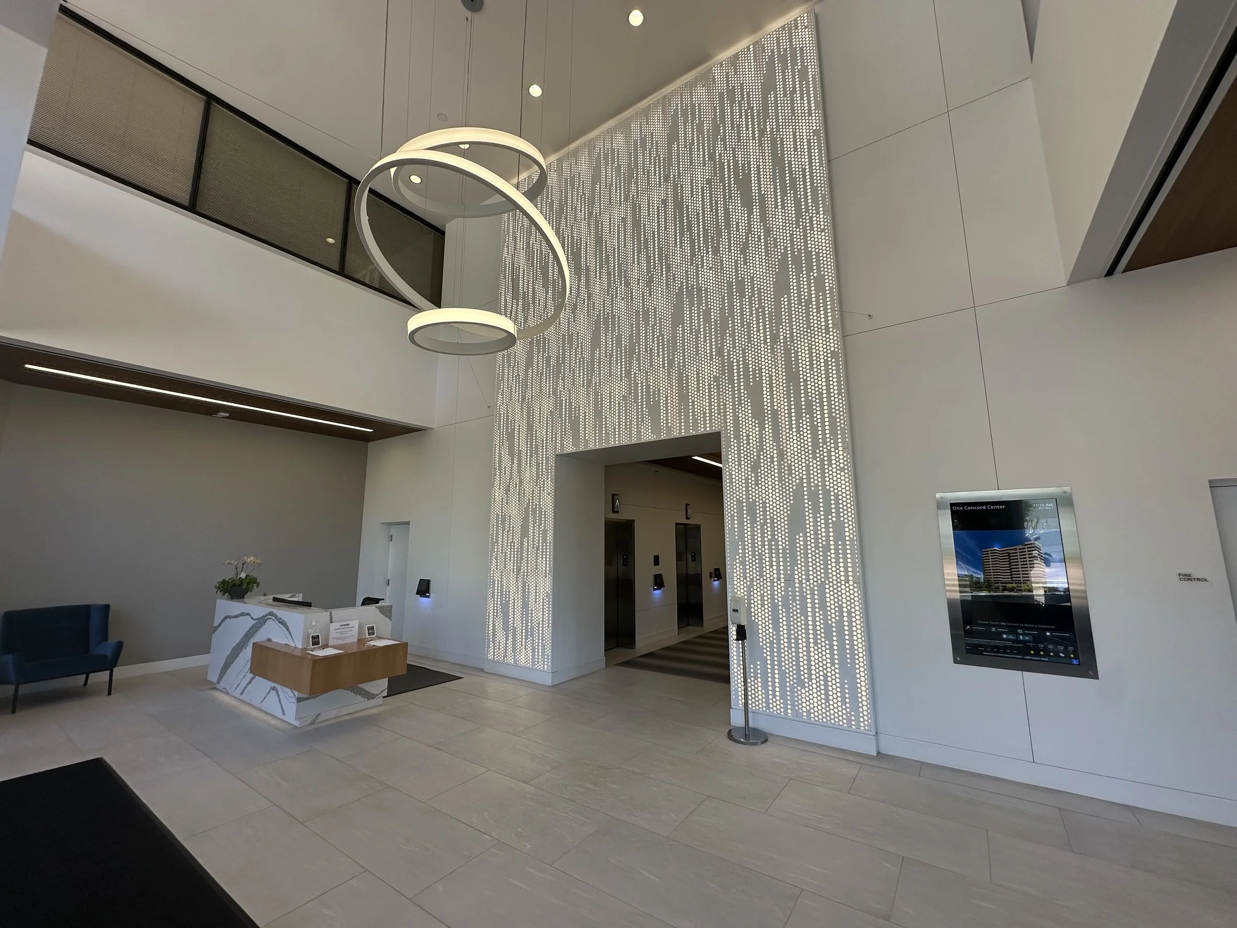 Lobby with modern lighting fixture, elevator doors, a hand sanitizer station, and a digital directory on the wall.