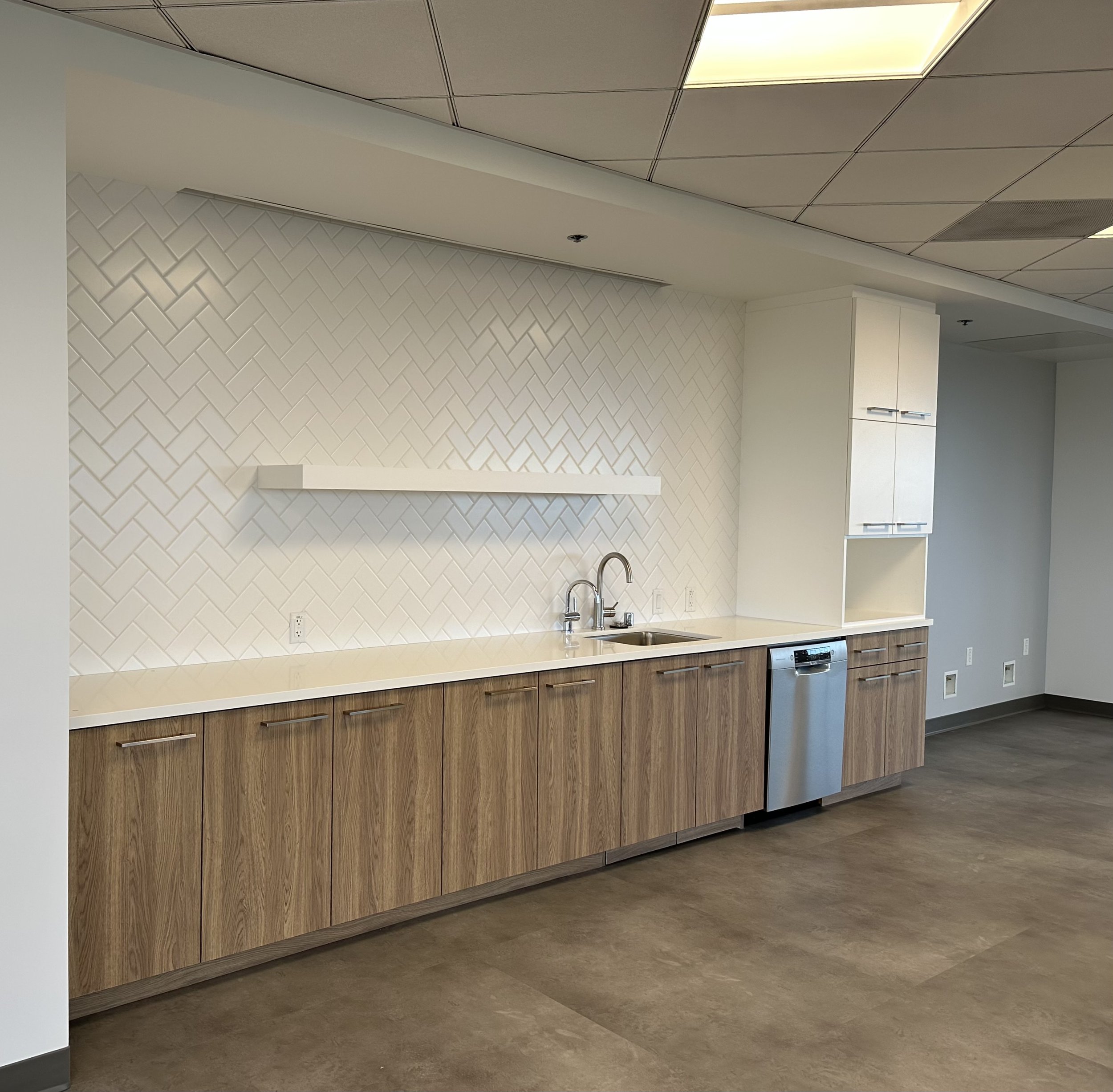 Modern kitchenette with a white tiled backsplash, wooden cabinets, a stainless steel dishwasher, and a double sink.