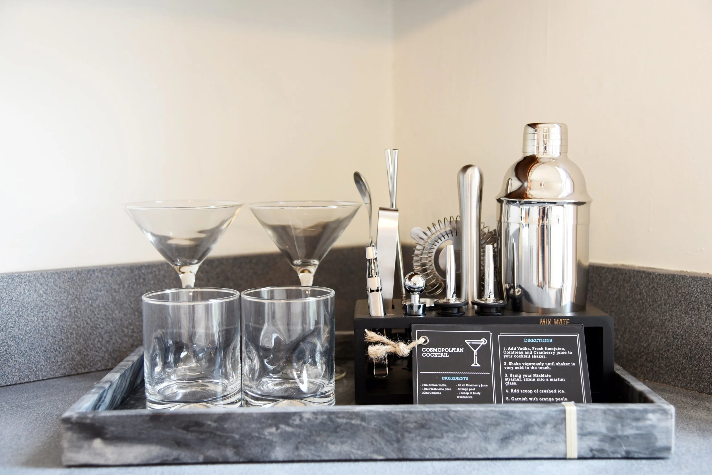 Barware set with cocktail making tools, glasses, and ingredients on a bar counter