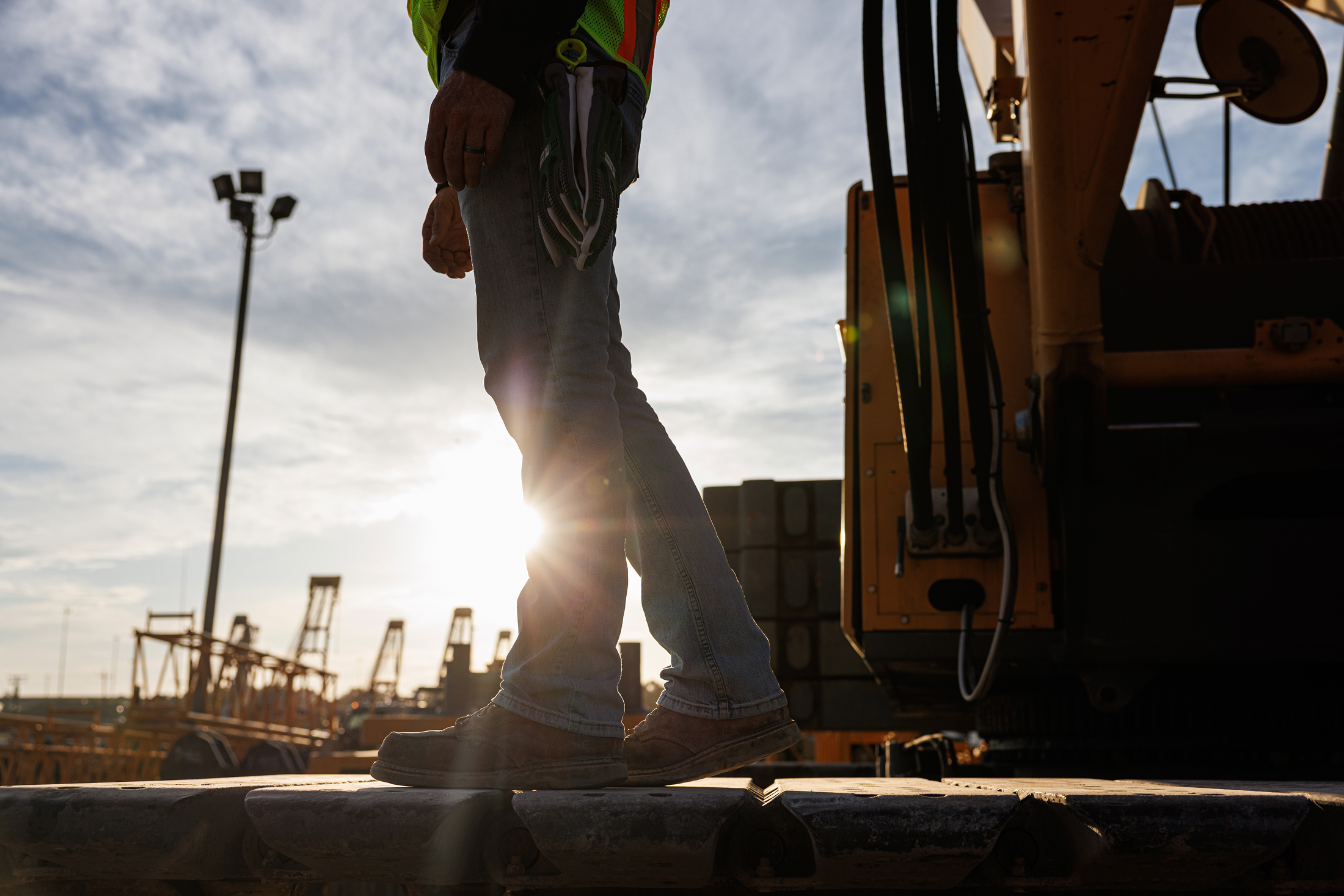 Silhouette of a construction worker standing on railway tracks at sunset, with construction equipment and cranes in the background.