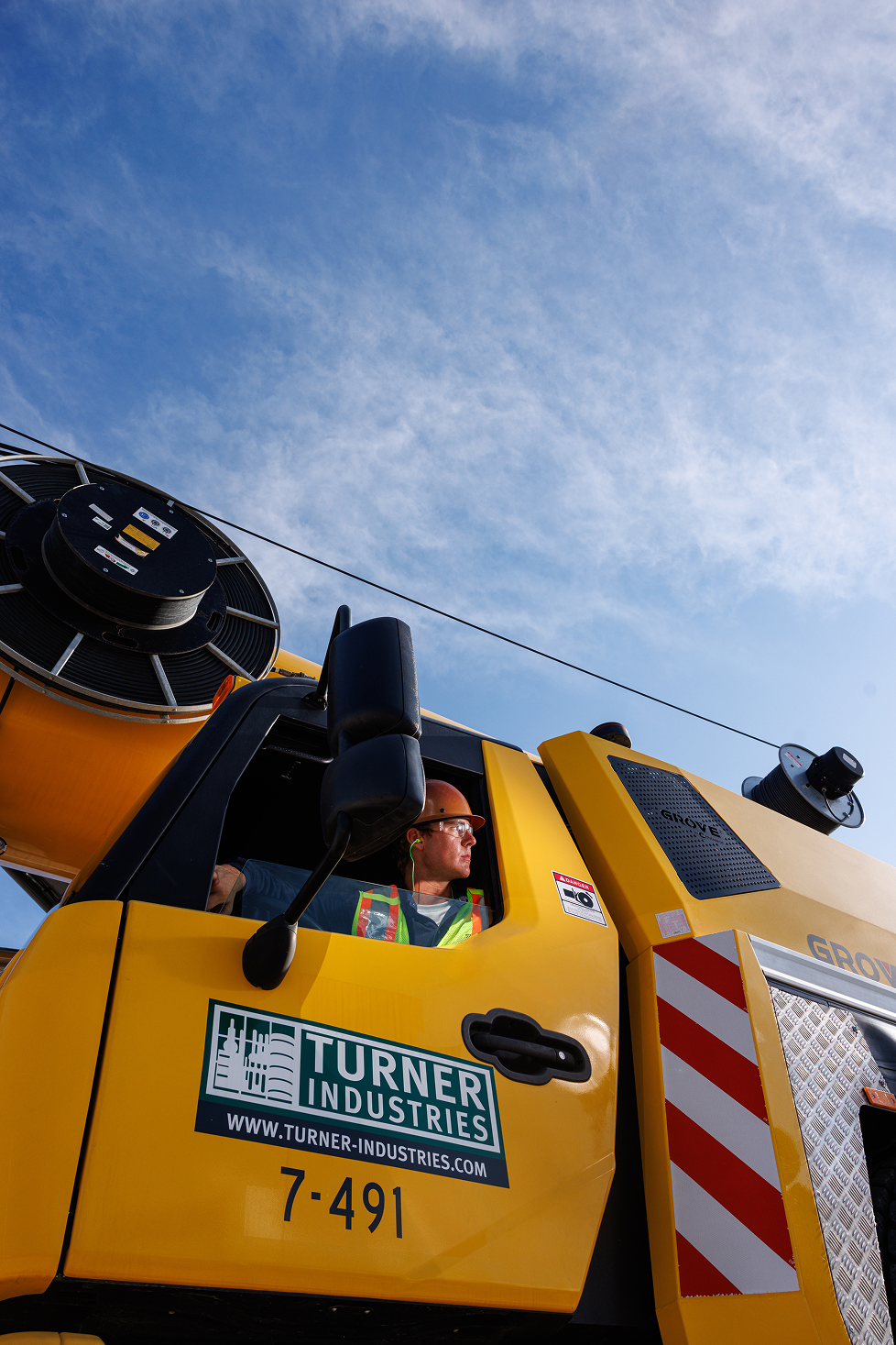 A yellow utility bucket truck with a worker inside wearing a hard hat and safety vest, operating equipment, against a blue sky background.