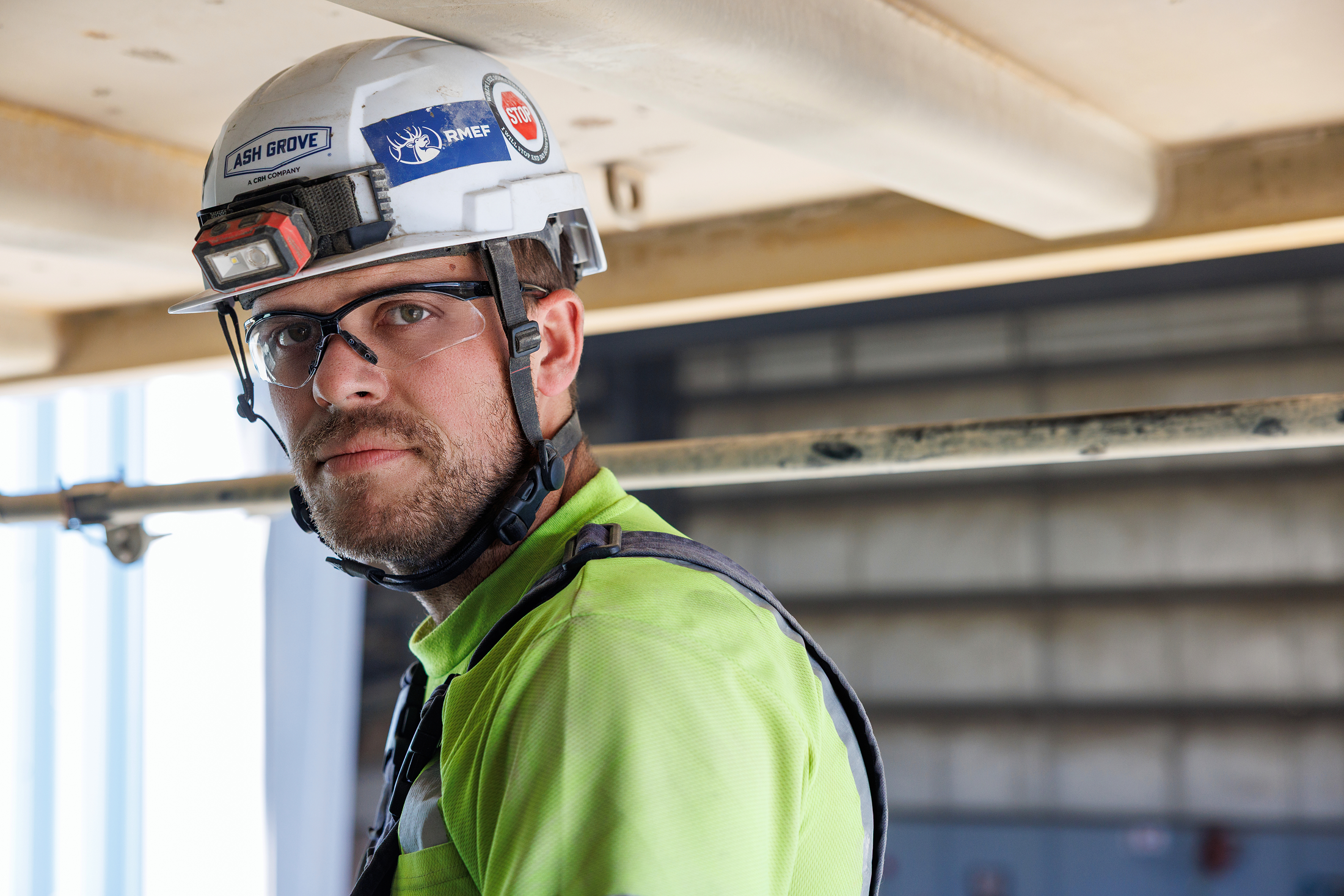Construction worker wearing a safety helmet, safety glasses, and high-visibility clothing at a construction site.