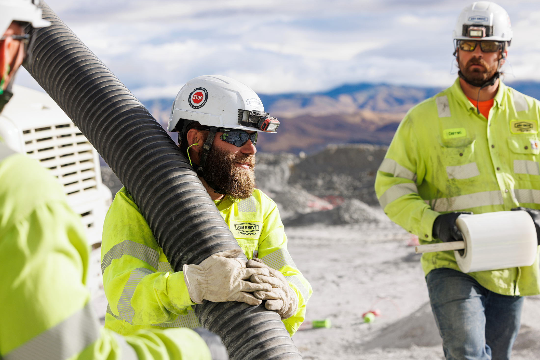 Construction workers in high-visibility jackets and helmets working outdoors with mountainous terrain in the background.