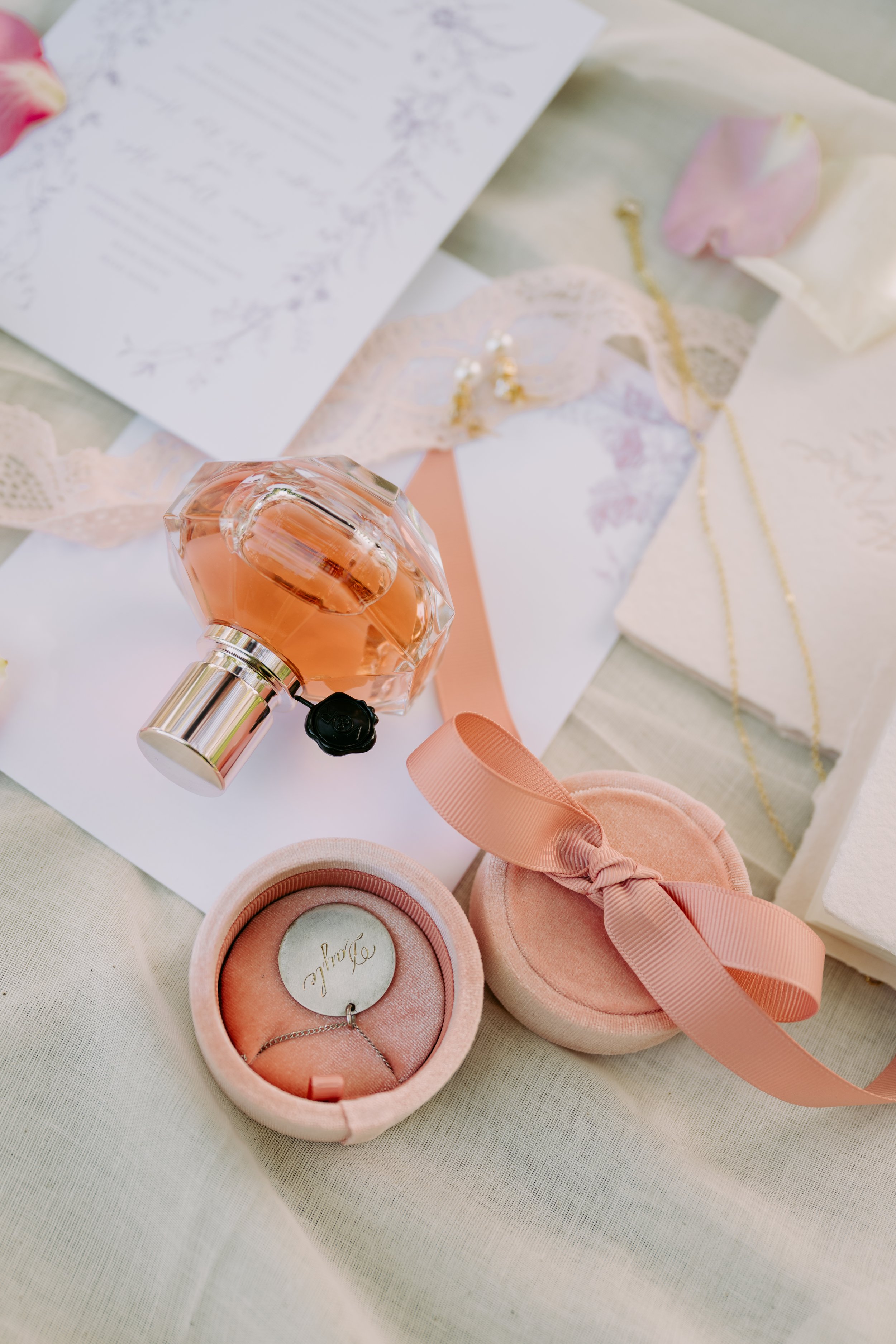 A collection of perfume, jewelry, and gift items on a table with pink and white decorations, likely for a special occasion.