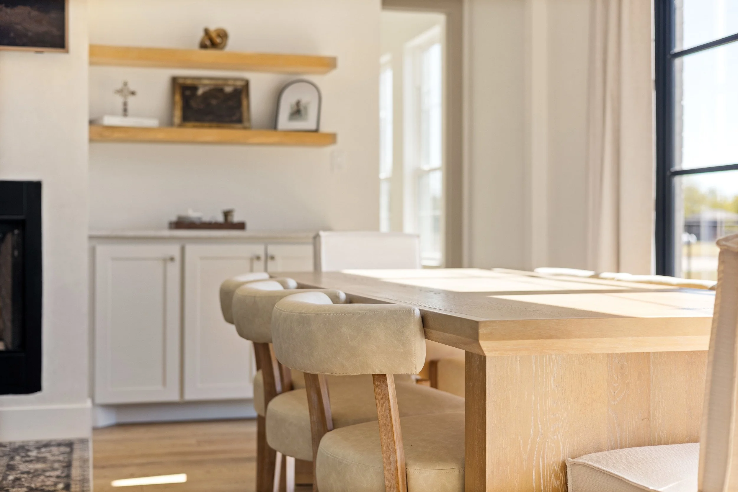 A dining area with a wooden table and beige upholstered chairs, bright natural light, and consistent decor in neutral tones.