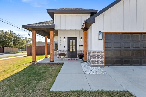 Front view of a modern house with a black front door, brick and white siding exterior, and a black garage door, with a concrete walkway and a grassy lawn.