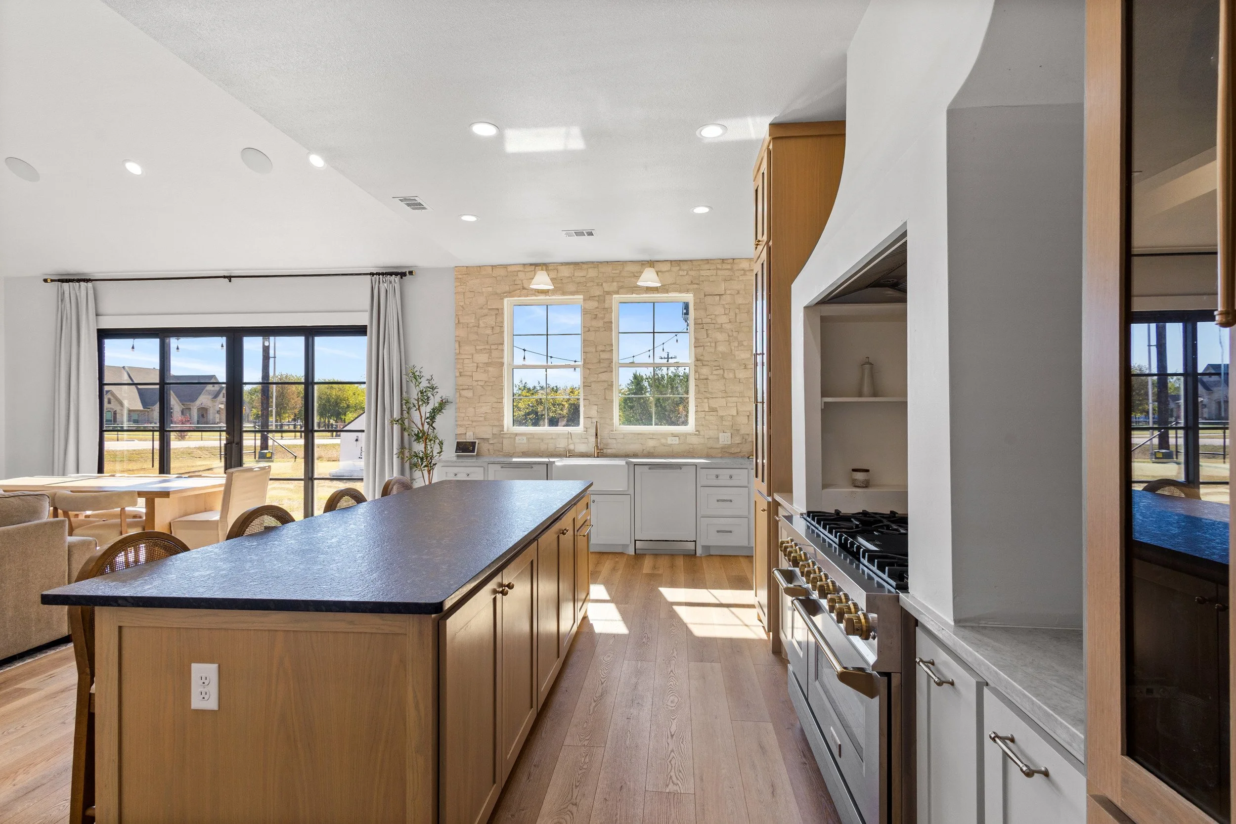 Open-concept kitchen and living area with large windows, wooden cabinetry, and a kitchen island.