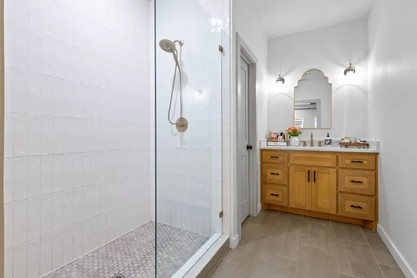 Bathroom with a glass-enclosed shower on the left and a wooden vanity with a mirror and flowers on the right.