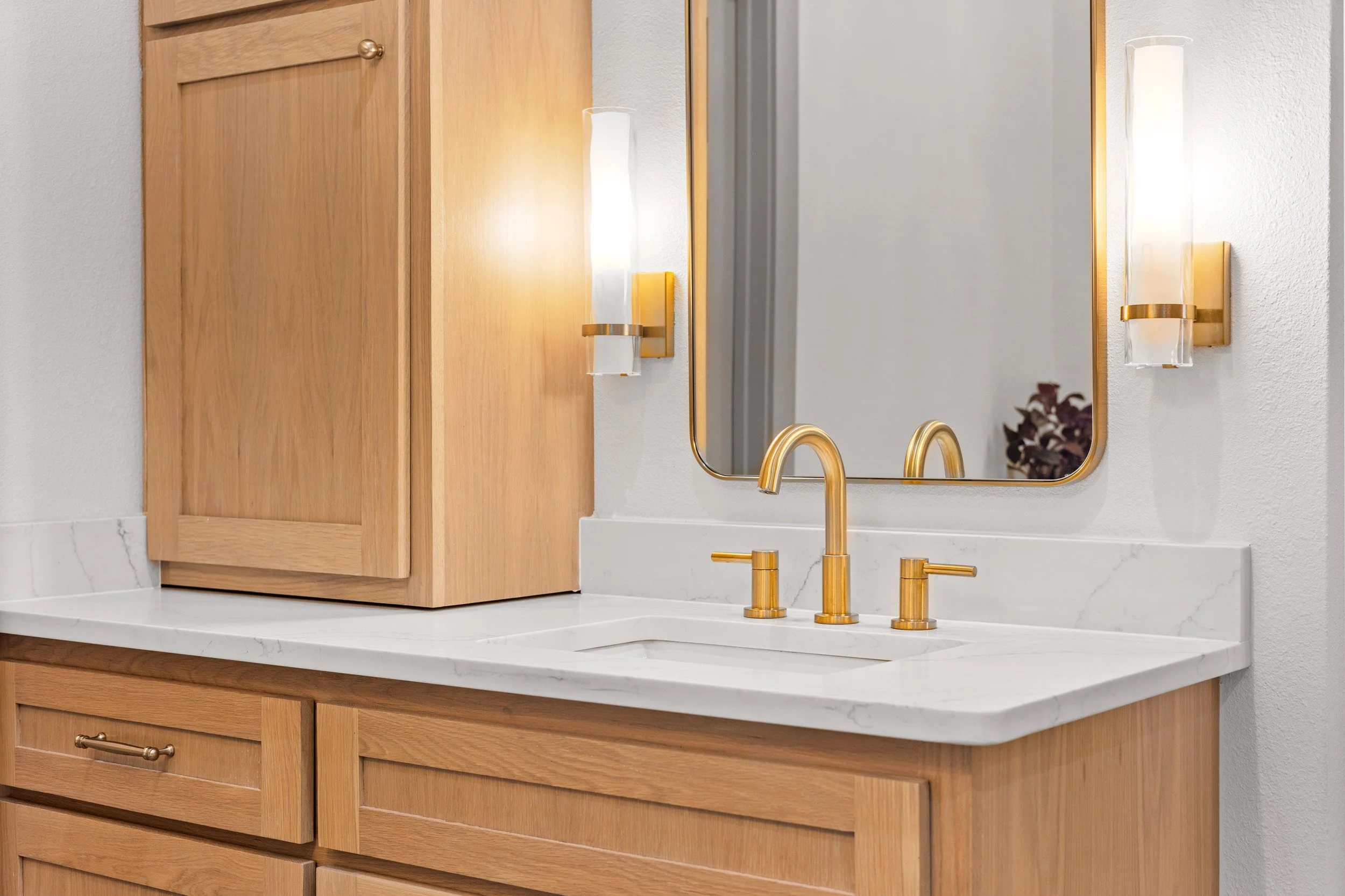 Wood bathroom vanity with a white quartz countertop, gold fixtures, a mirror, and two wall sconces.