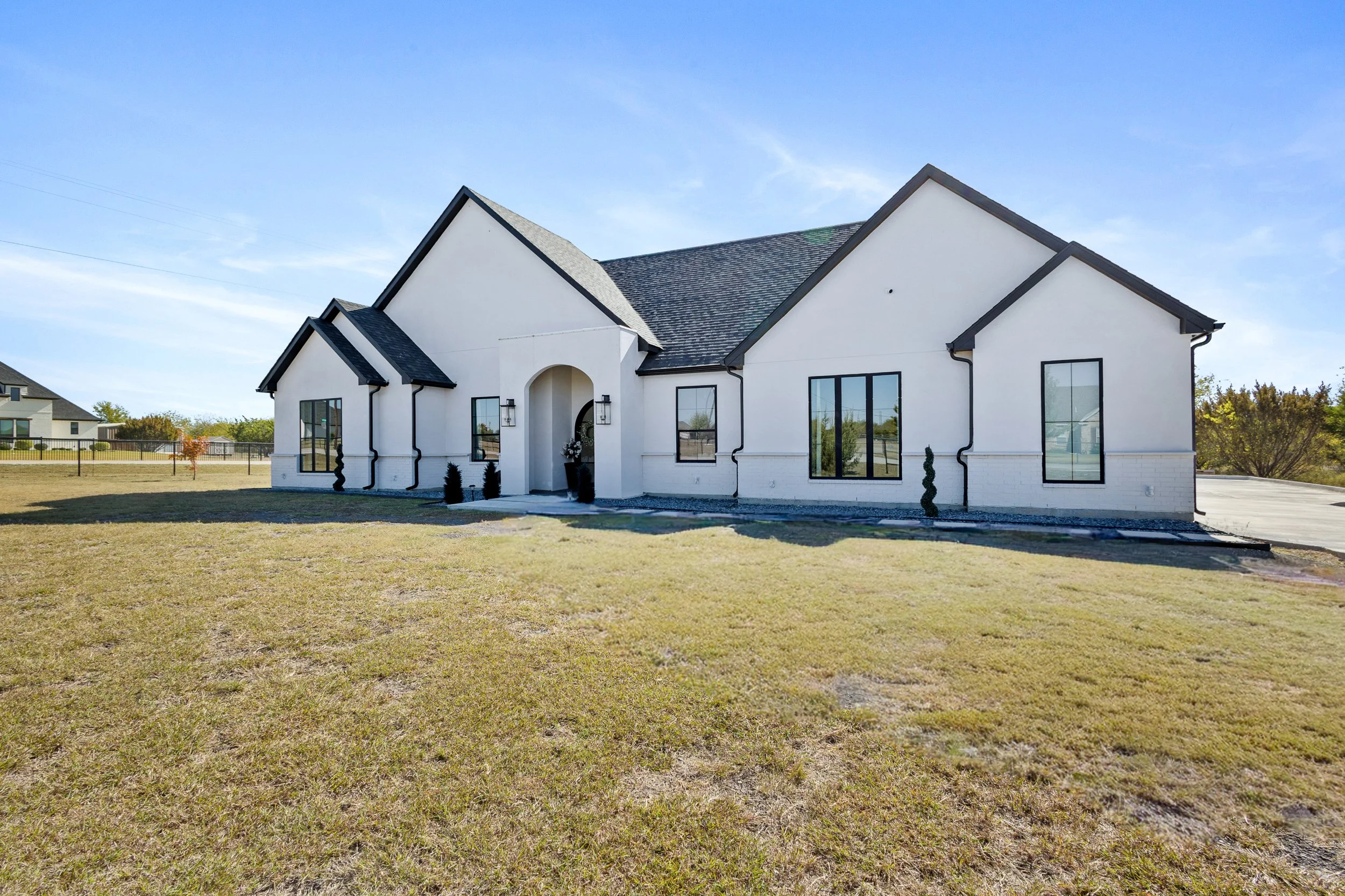 A newly built white house with black roof and window frames on a grassy lawn.
