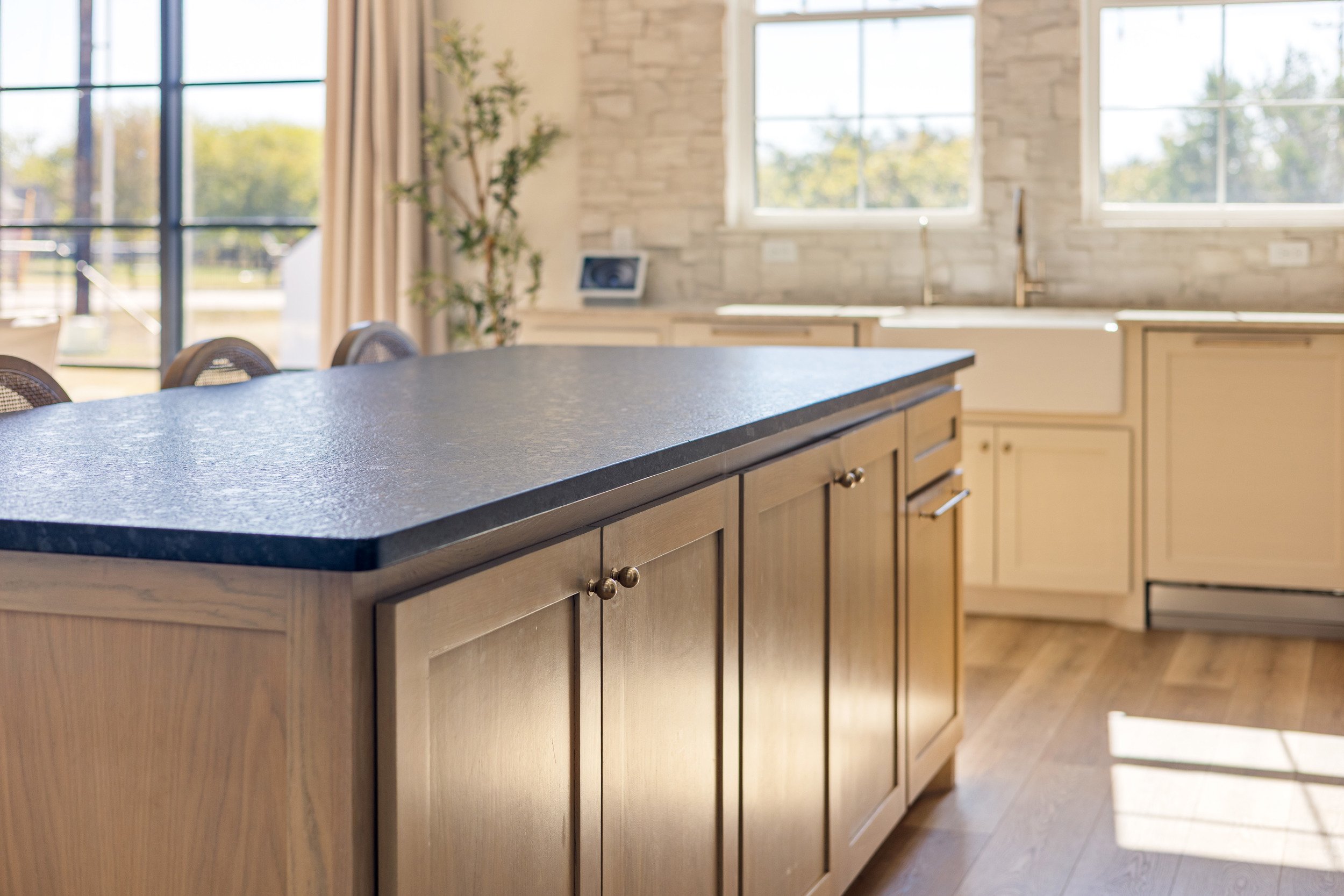 Modern kitchen with wooden cabinets, a large black countertop island, and bright natural light from large windows.