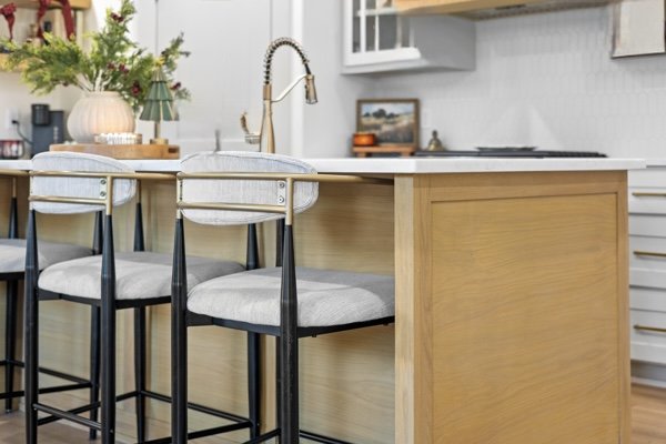 Kitchen island with three bar stools, white countertop, and light wood base in a modern kitchen