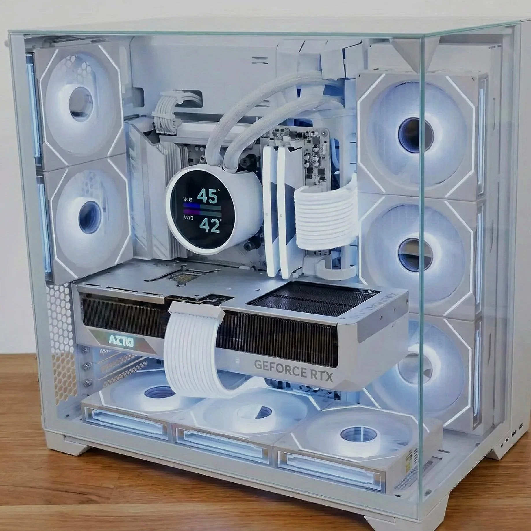 A custom-built computer inside a glass case with white components, RGB lighting, multiple fans, a prominent graphics card labeled 'GEFORCE RTX,' and a circular display showing Celsius temperature readings.