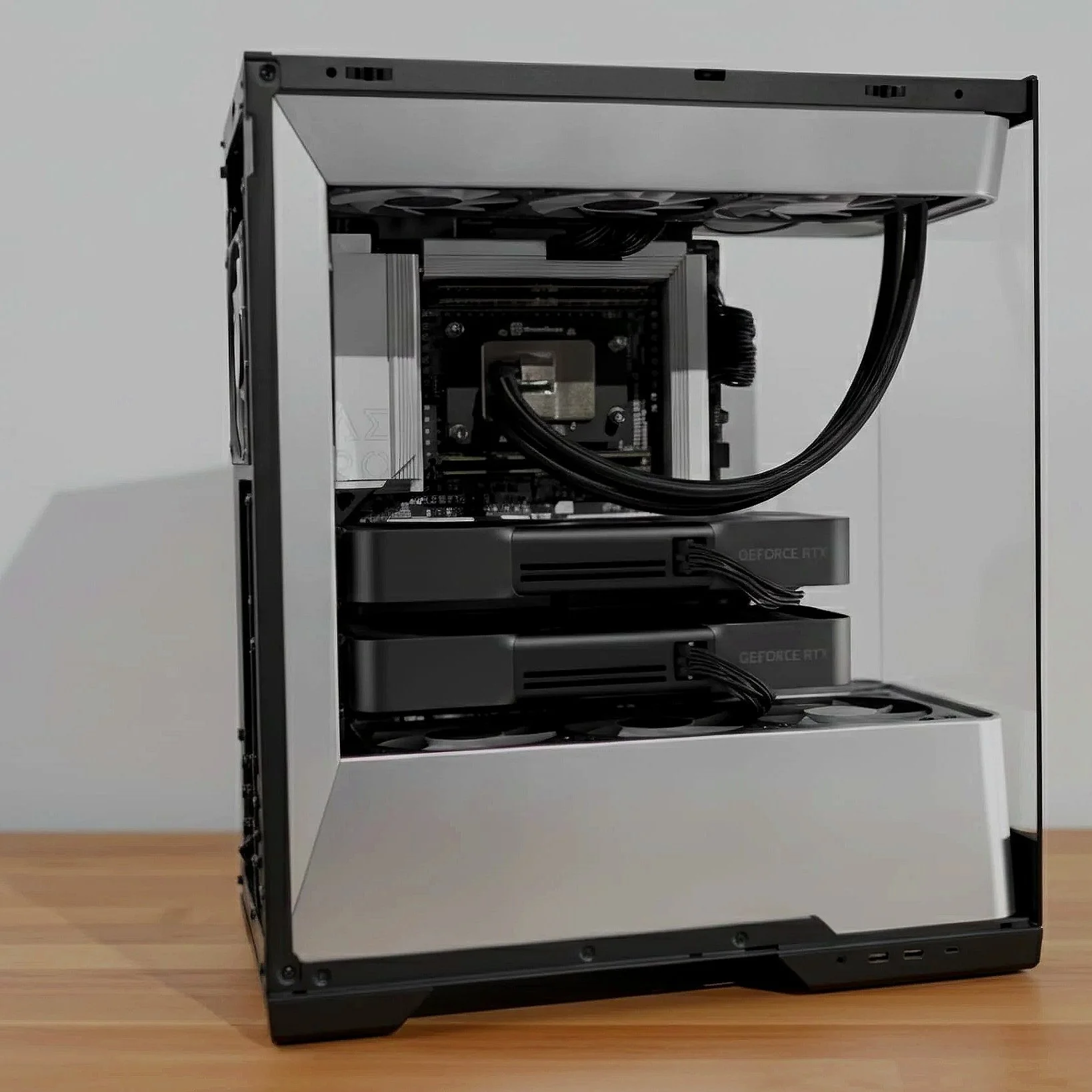 Open computer case with internal components, including graphics cards, cooling system, and cables, placed on a wooden surface against a plain wall.