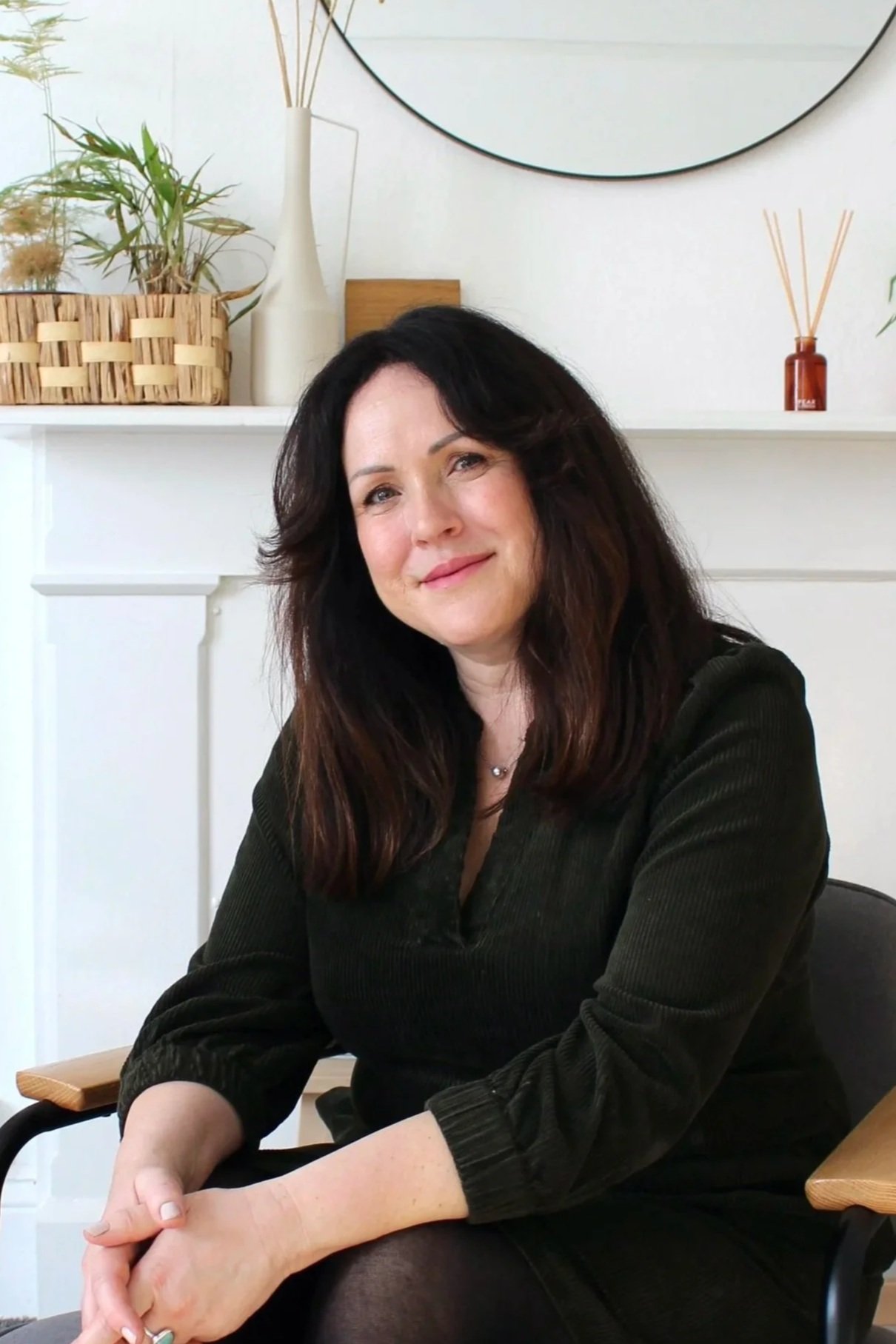 Ellen Baldwin sitting on a chair with wooden and black accents in her therapy room.