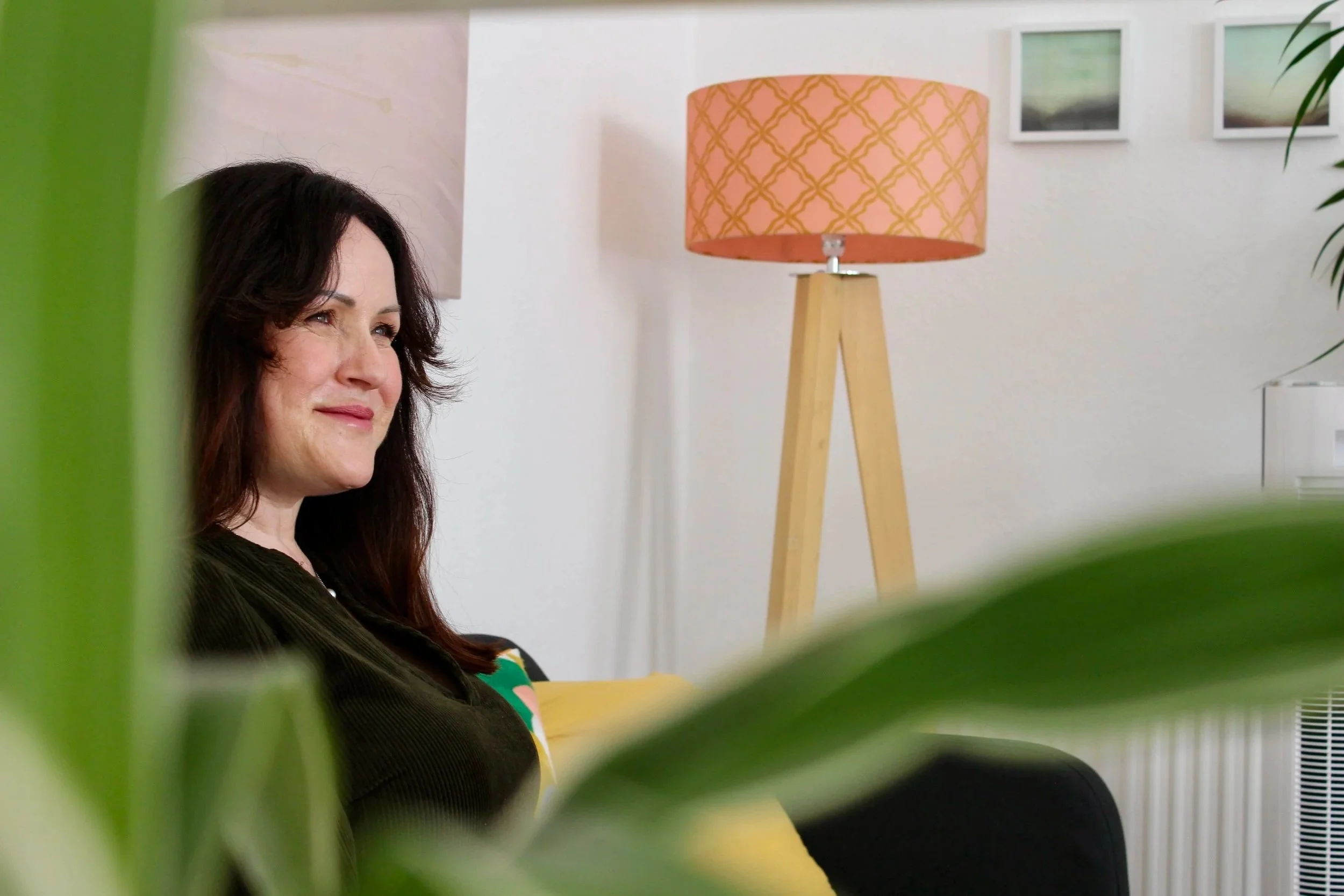 Ellen Baldwin sitting on a couch with green plants in the background.
