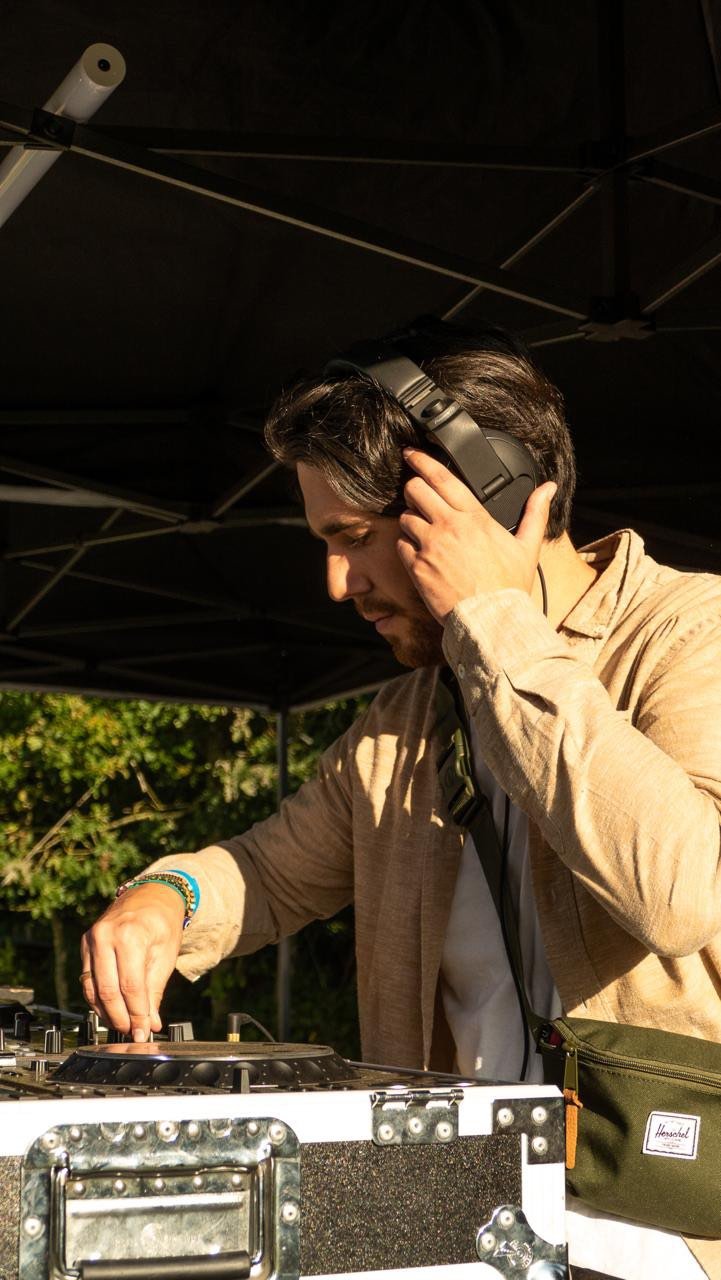 Un dj portant un casque, manipulant du matériel de musique sous une tente en extérieur.