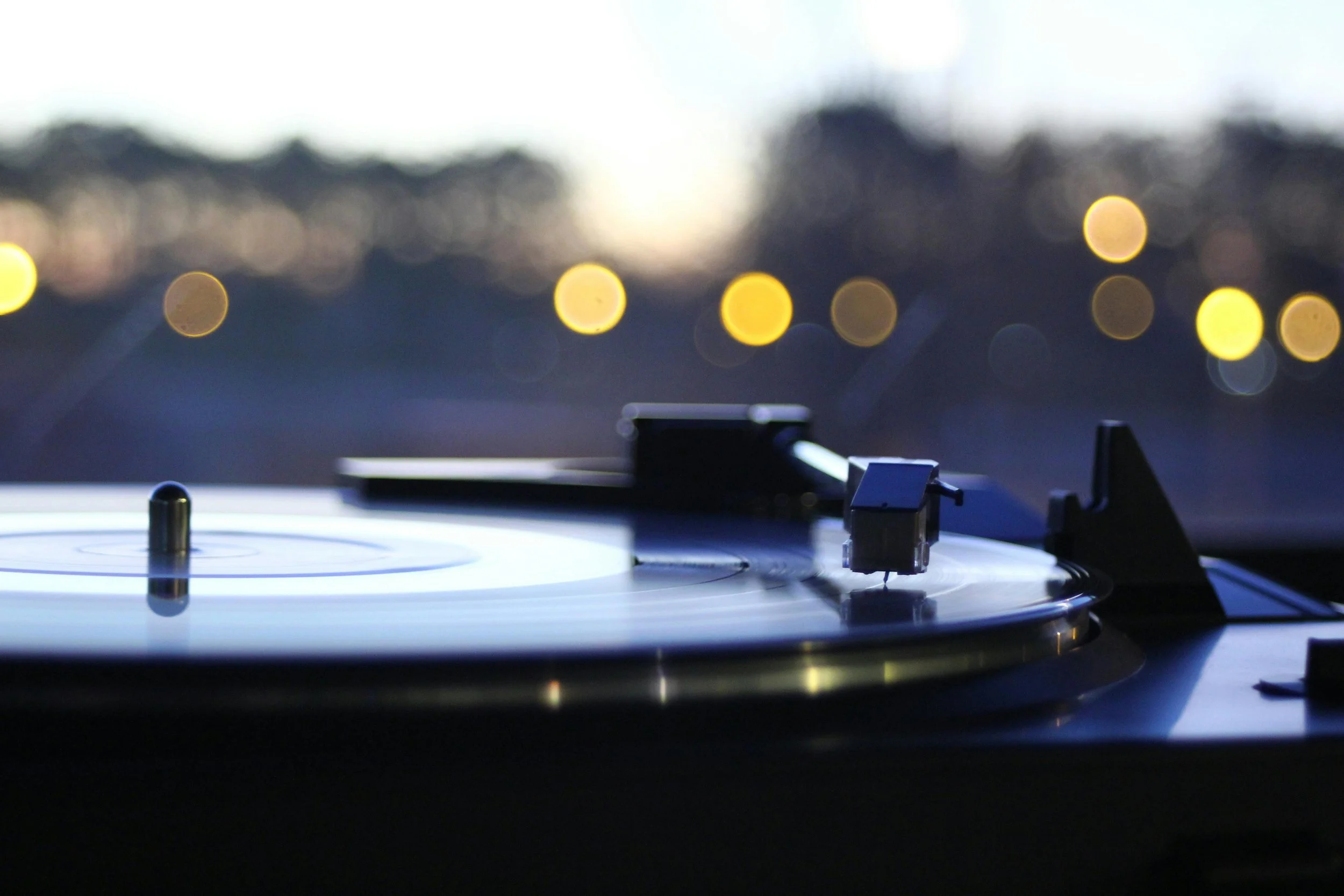Plateau de DJ avec platine vinyle en gros plan, fond flou avec lumières de ville créant un effet bokeh au crépuscule.