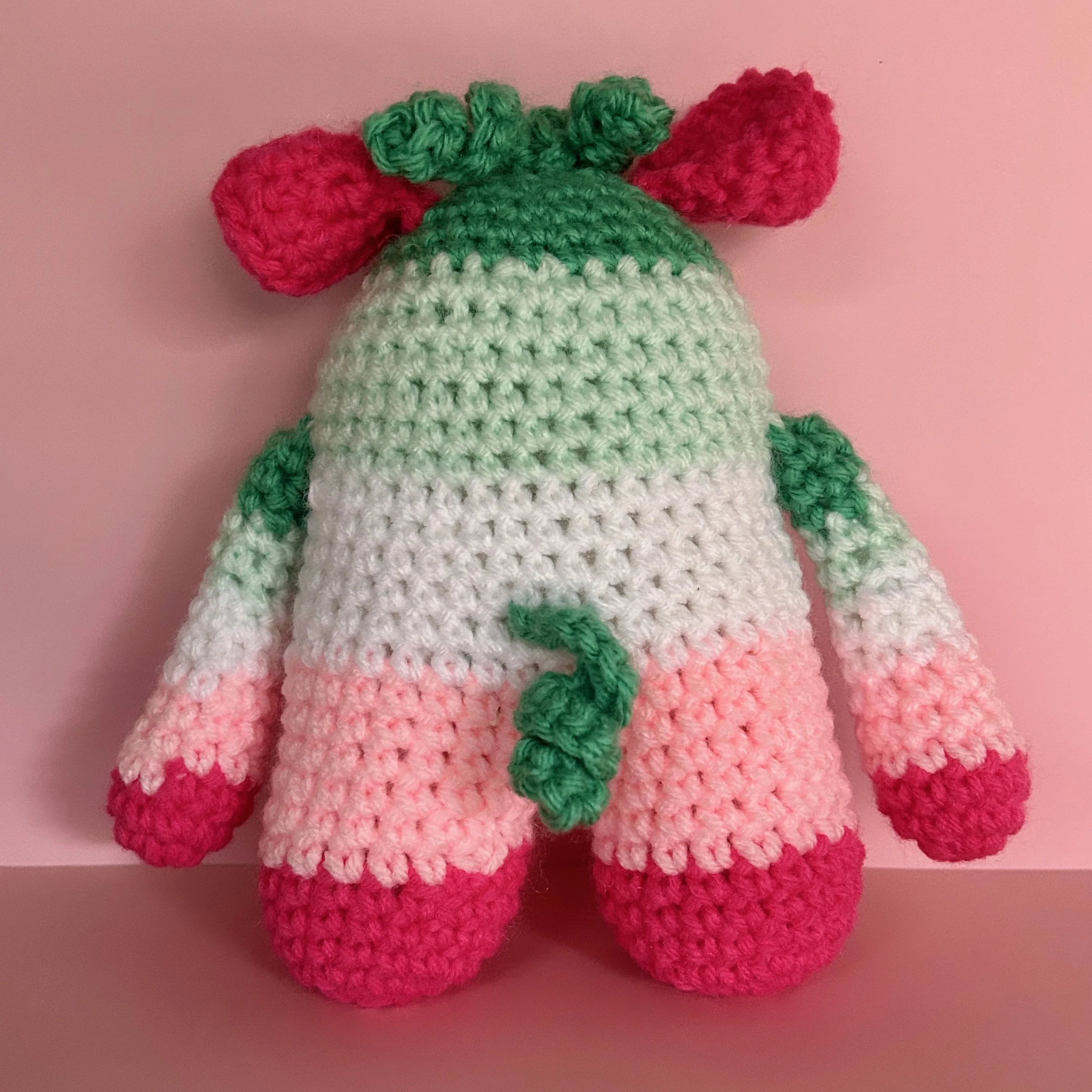 back of green, white, and pink striped monster with jade green squiggly hair and tail and bright pink folded ears