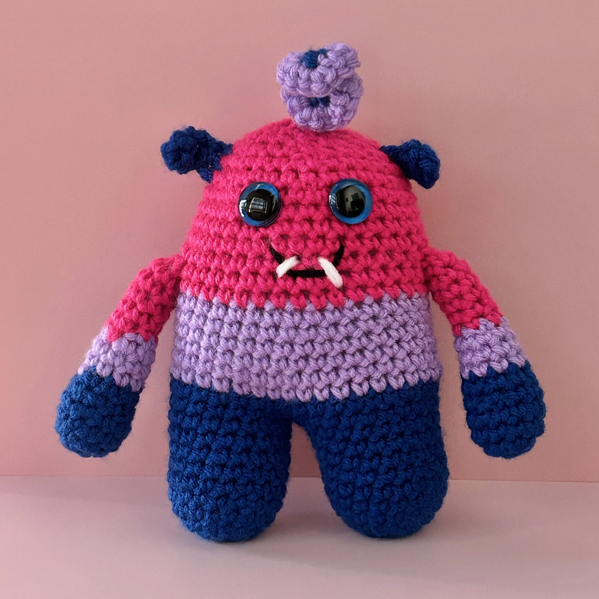 friendly monster plushie bisexual pride flag magenta lavender royal blue stripes blue googly eyes blue ears purple squiggle hair smiling with 2 teeth
