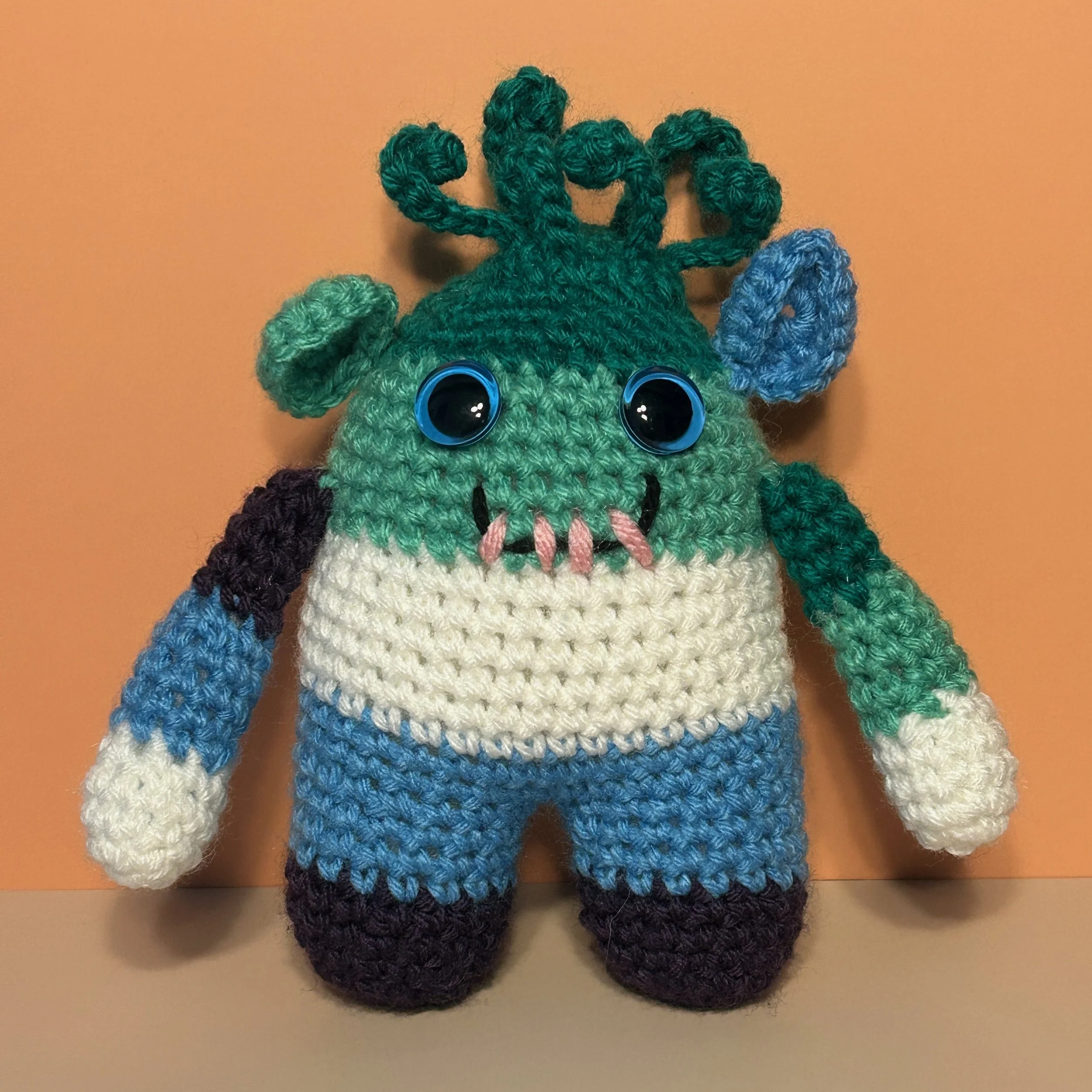 Jack green jade white light blue indigo striped monster with medusa-style hair, round ears, light blue googly eyes, smiling with four teeth