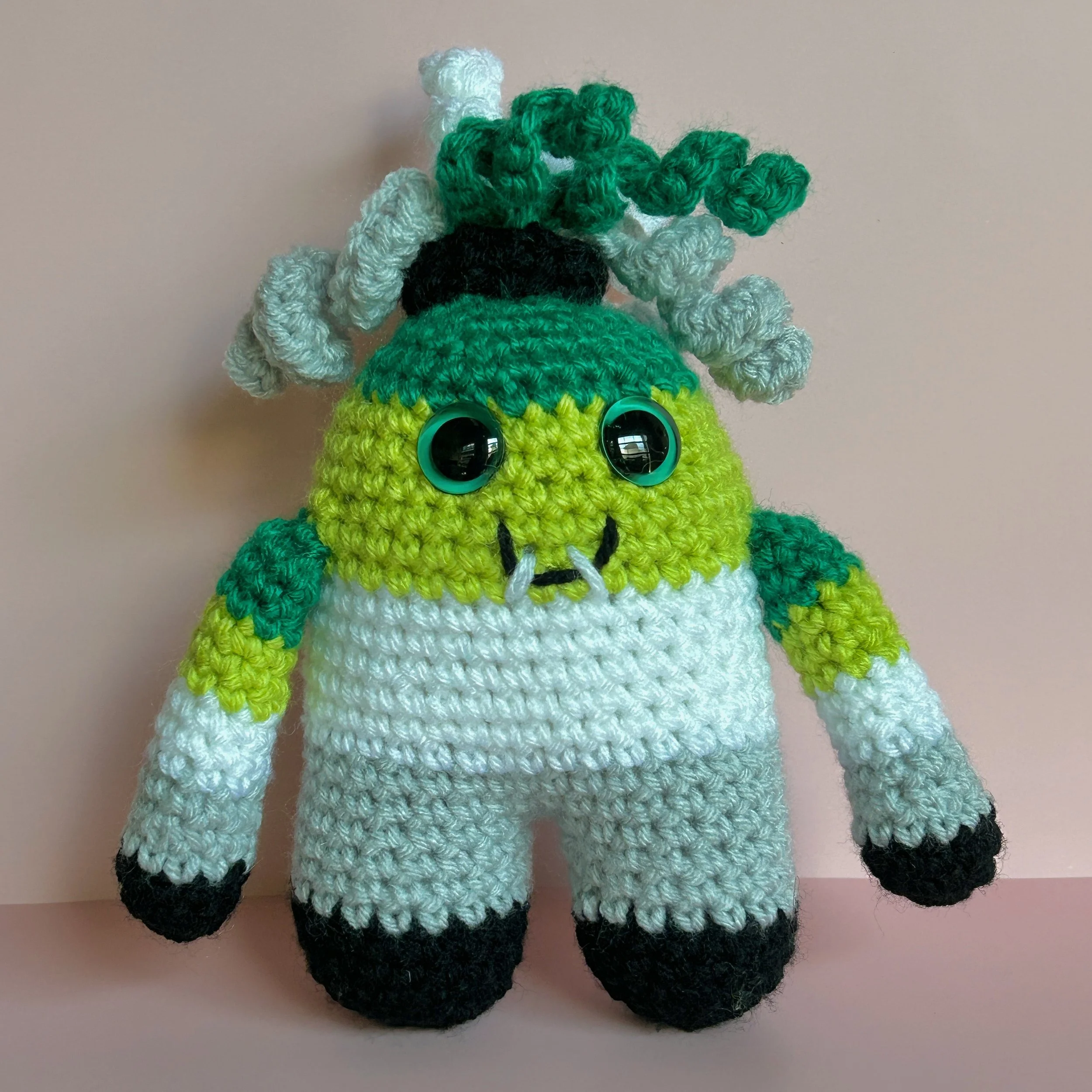 friendly green, light green, white, gray, black striped monster with white, grey, green curly hair in black scrunchie, green googly eyes smiling with 2 teeth