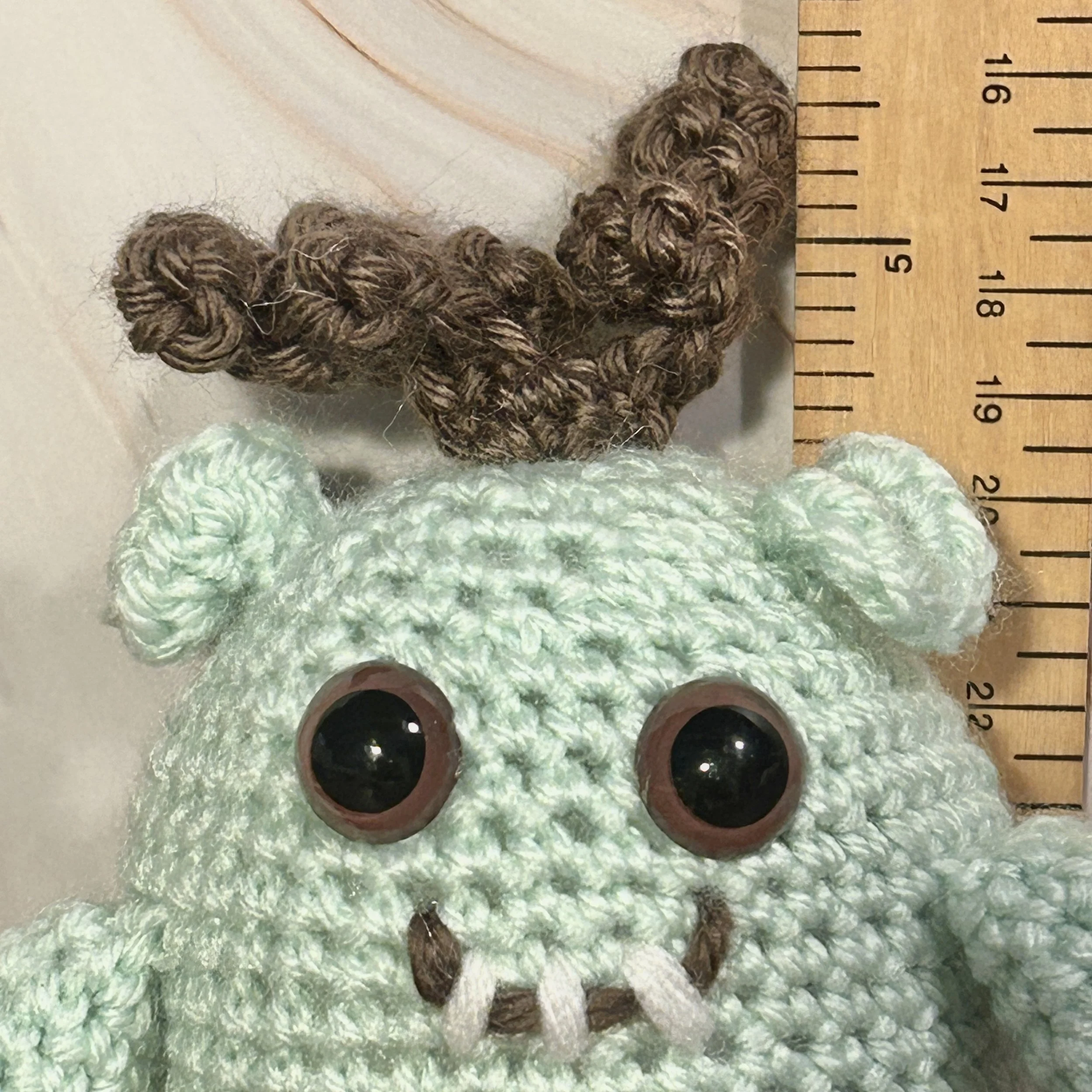 Cocominty closeup of face mint green monster curly brown hair brown googly eyes smiling with three teeth next to ruler about 4-1/2 inches tall