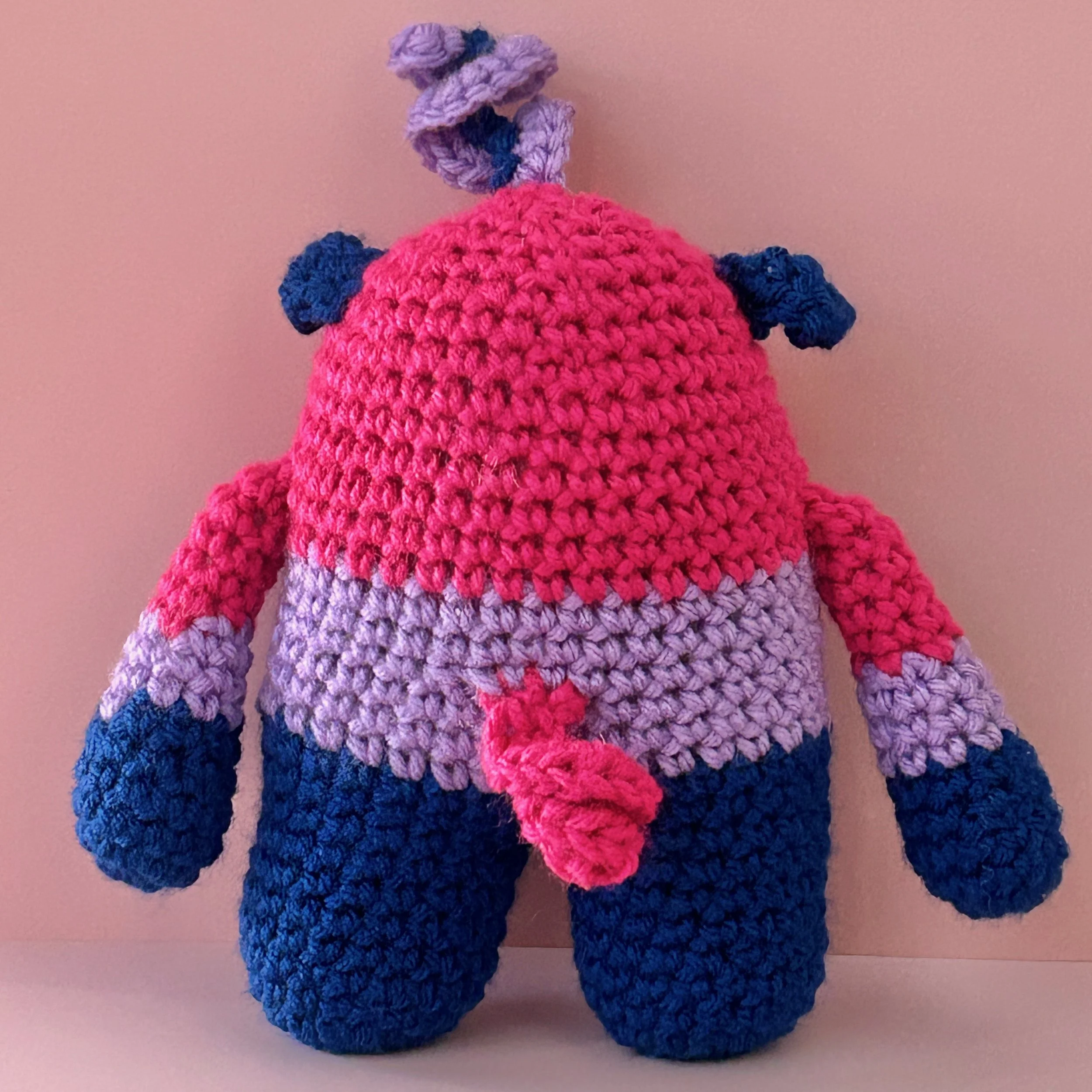 back of monster plushie bisexual pride flag magenta lavender royal blue stripes purple squiggle hair curly pink tail