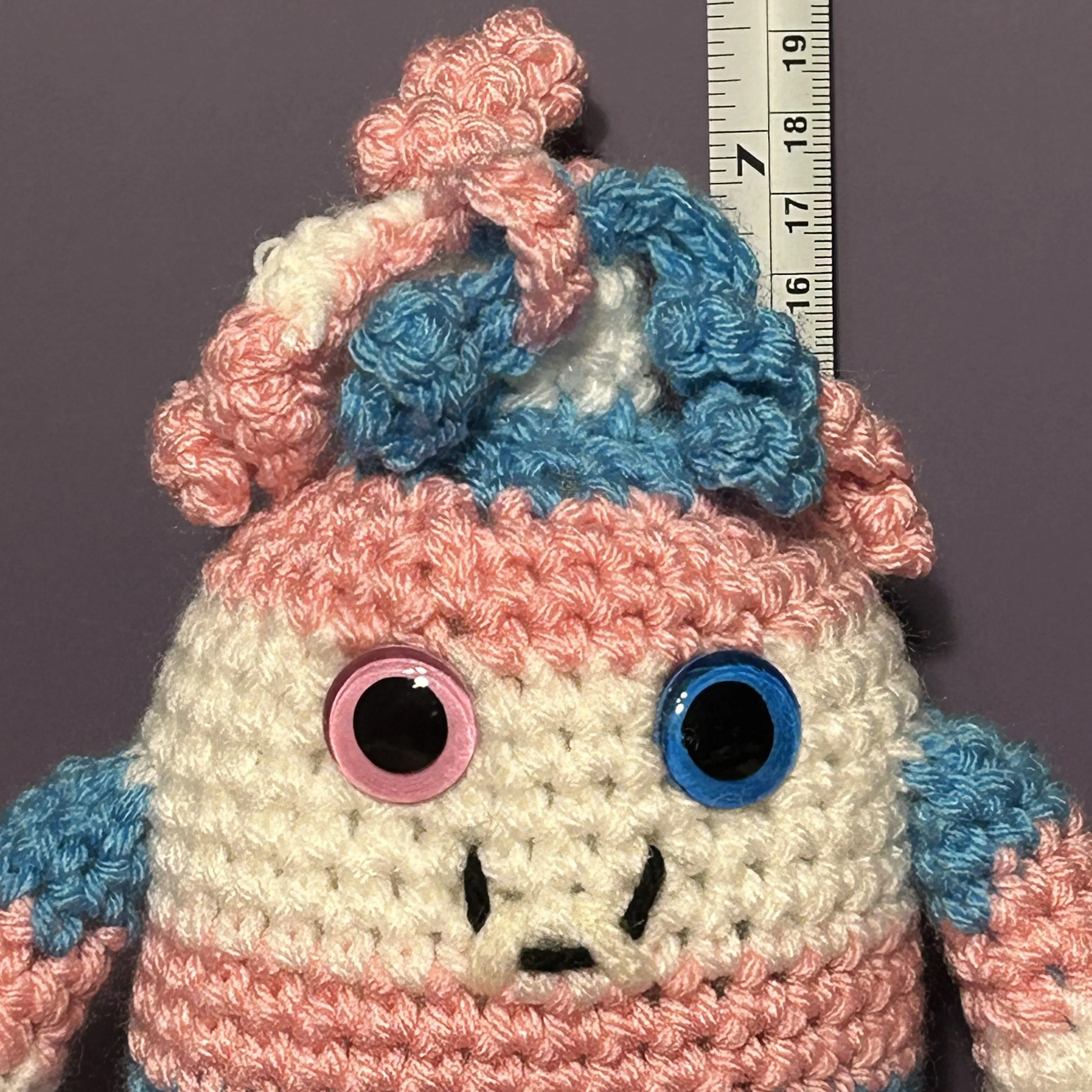 Mel light blue pink and white striped monster with mass of pink, blue, and white curly hair, one pink and one blue googly eye, smiling with 2 teeth in front of ruler, body about 6 inches tall (Copy)
